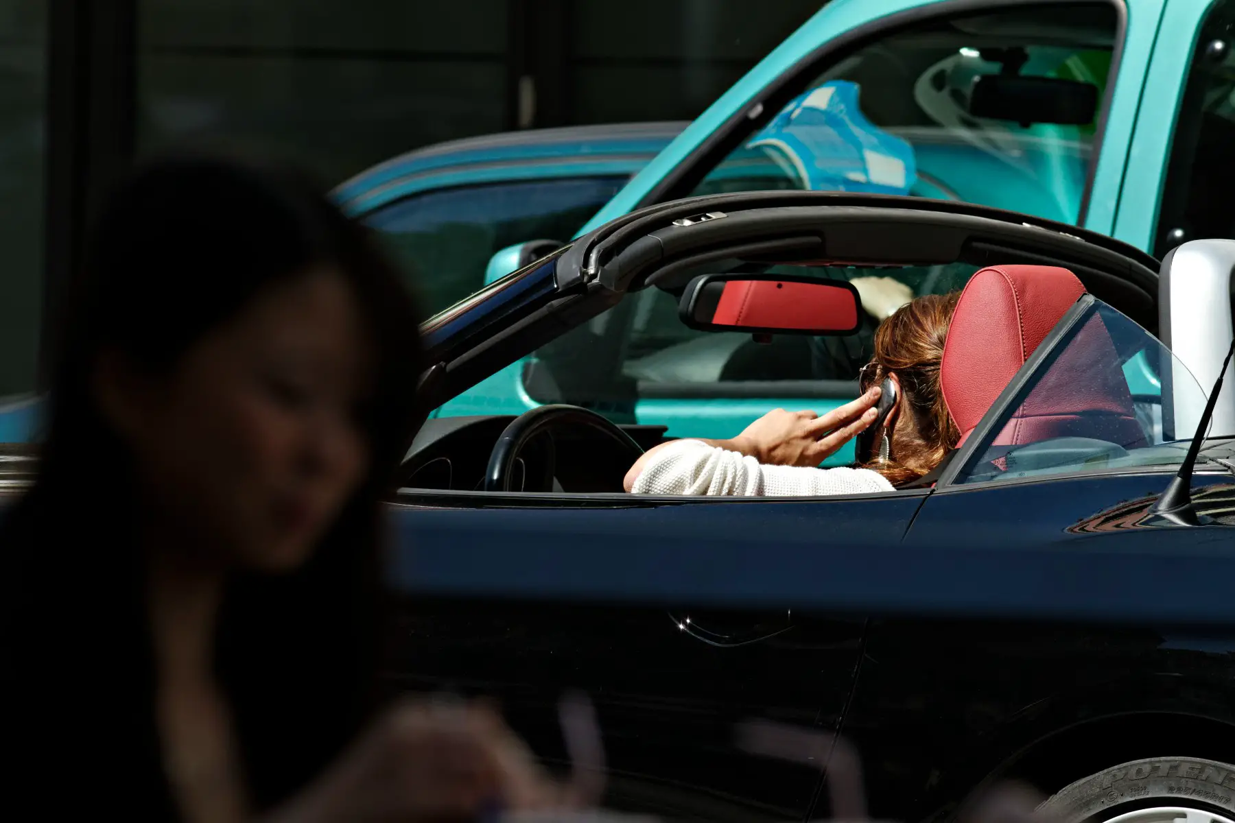 Woman talking on a mobile phone whilst driving a convertible car.
