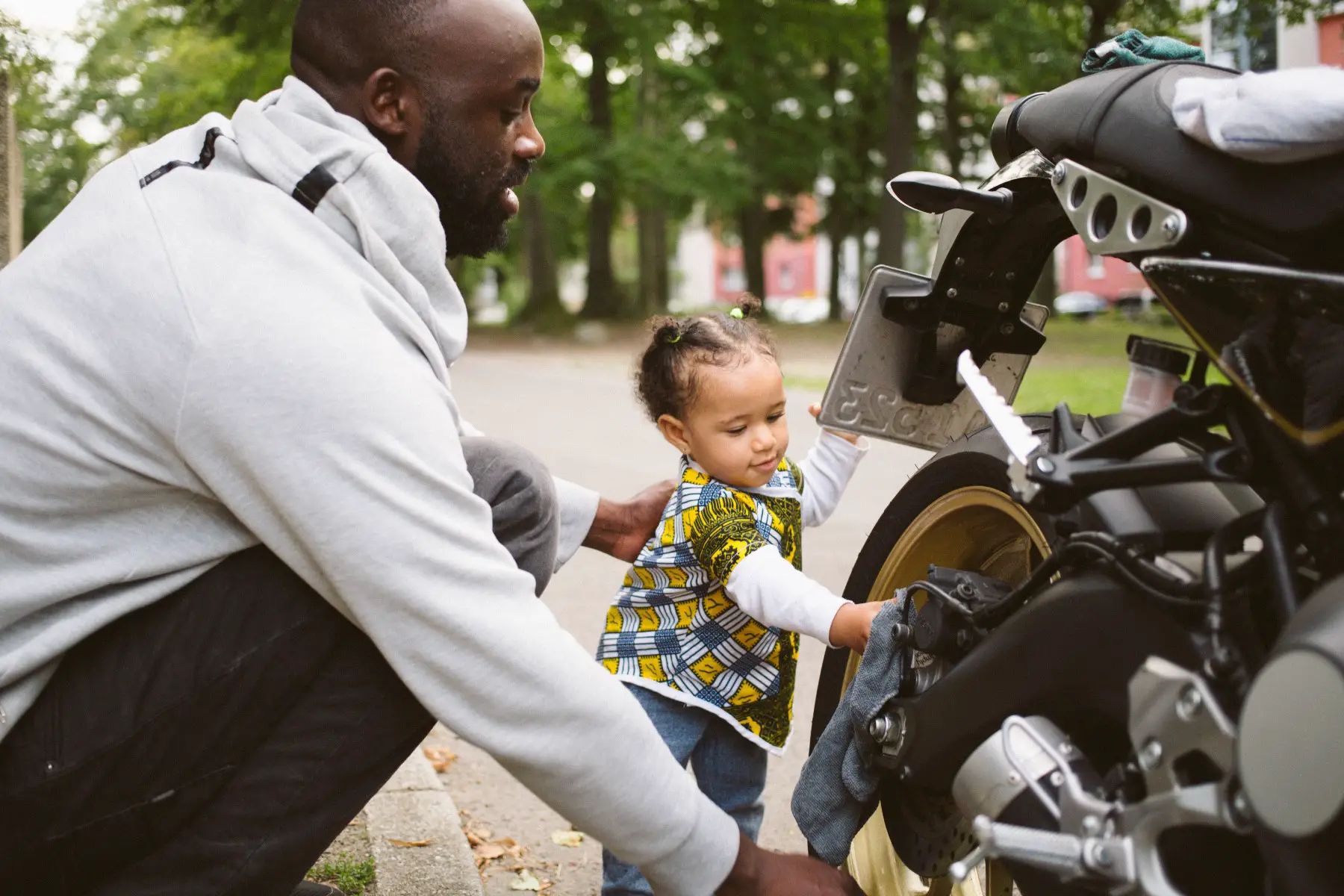 Father helping a baby clean a motorcycle.