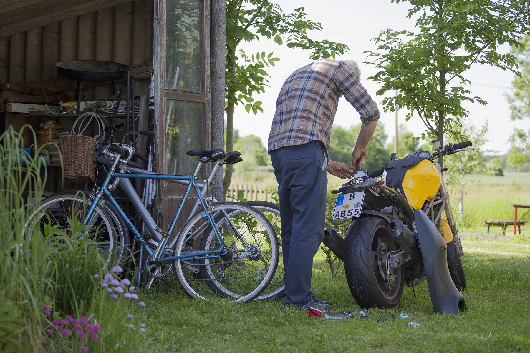Rear view of an older man repairing motorcycle at yard, German license plate clearly visible