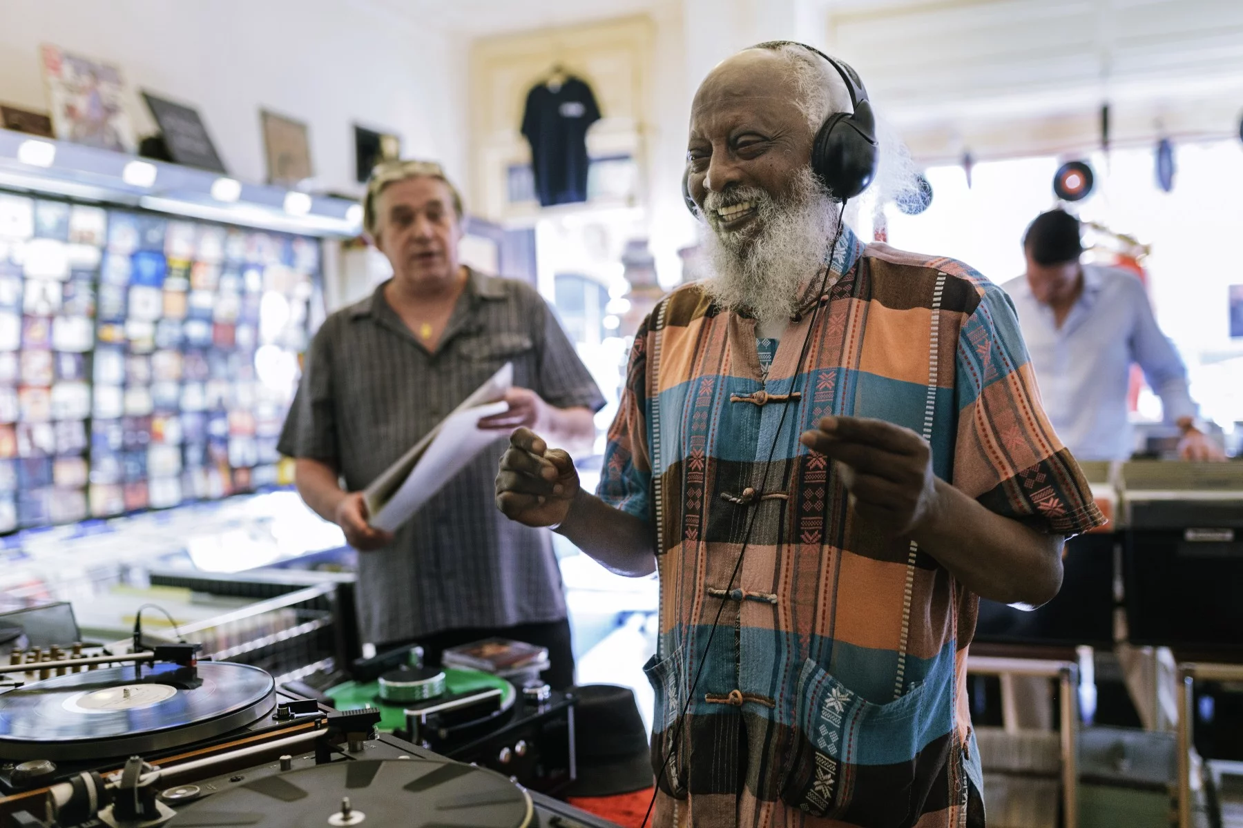 Elderly man laughing while listening to music in a record store. He is wearing headphones and snapping his fingers.