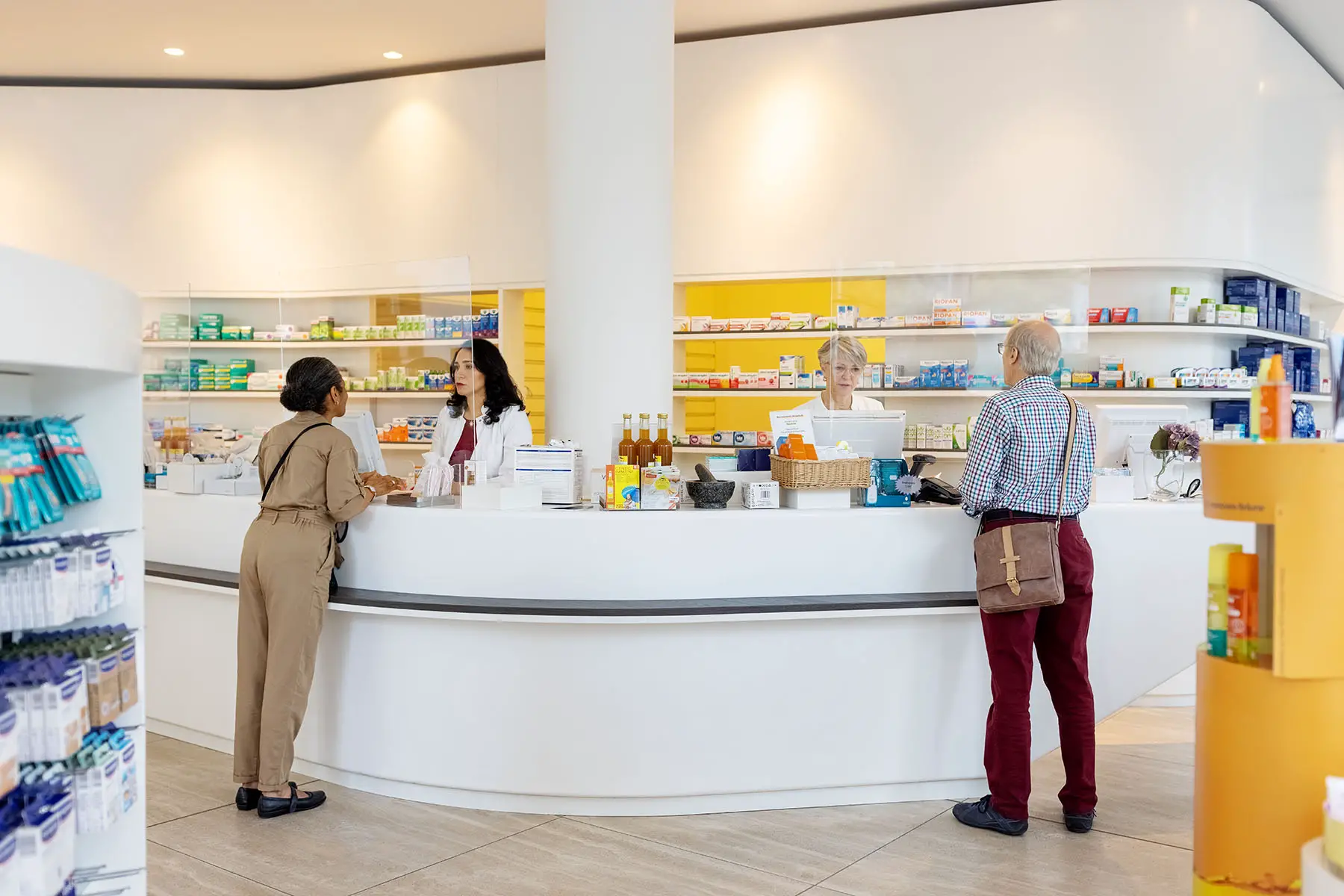 Two pharmacists standing behind the counter and assisting customers in a pharmacy store.