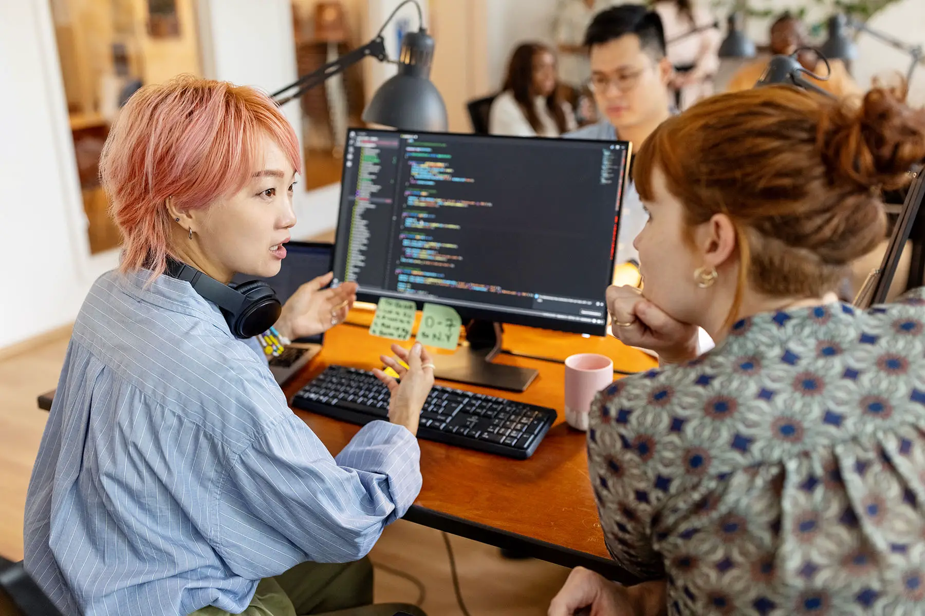 Two women software developers having a discussion while sitting behind a computer at a desk in the workplace.
