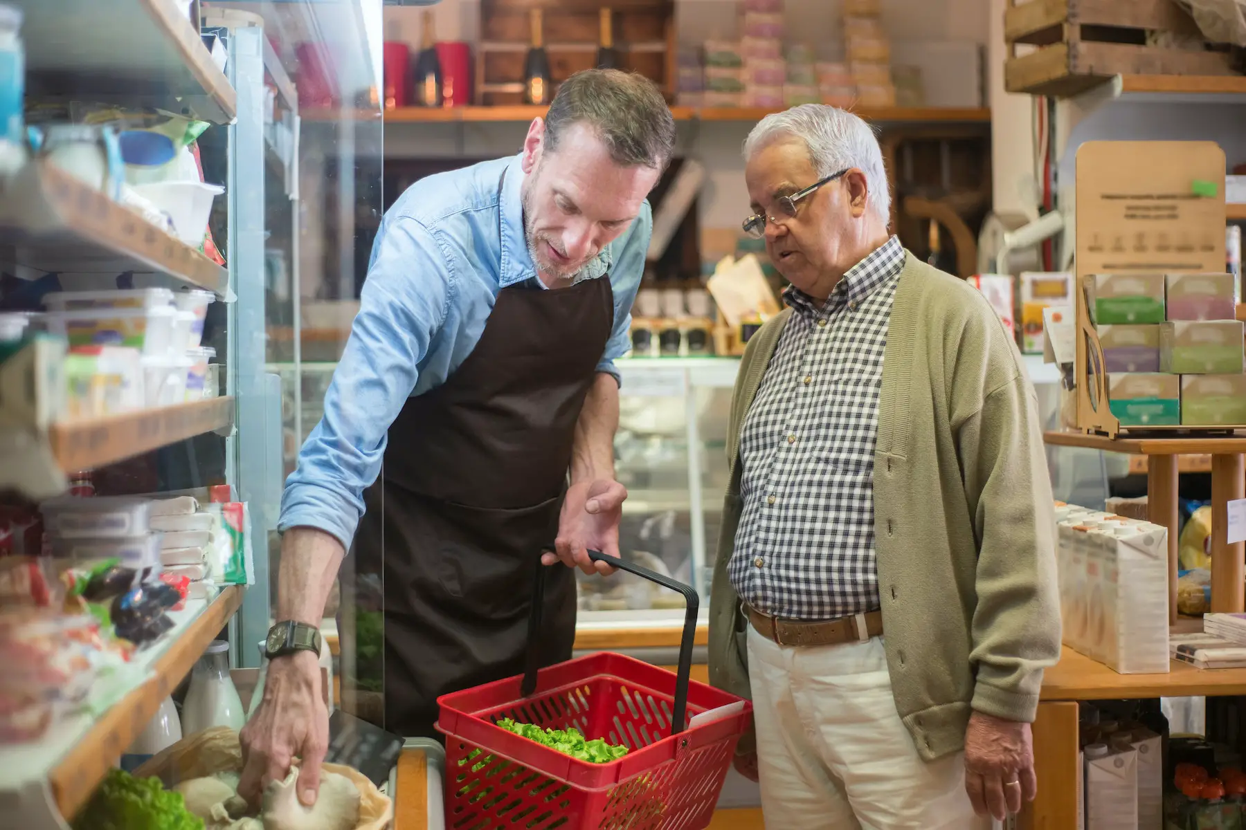 In an organic supermarket, an attendant helps an older customer looking for fresh produce