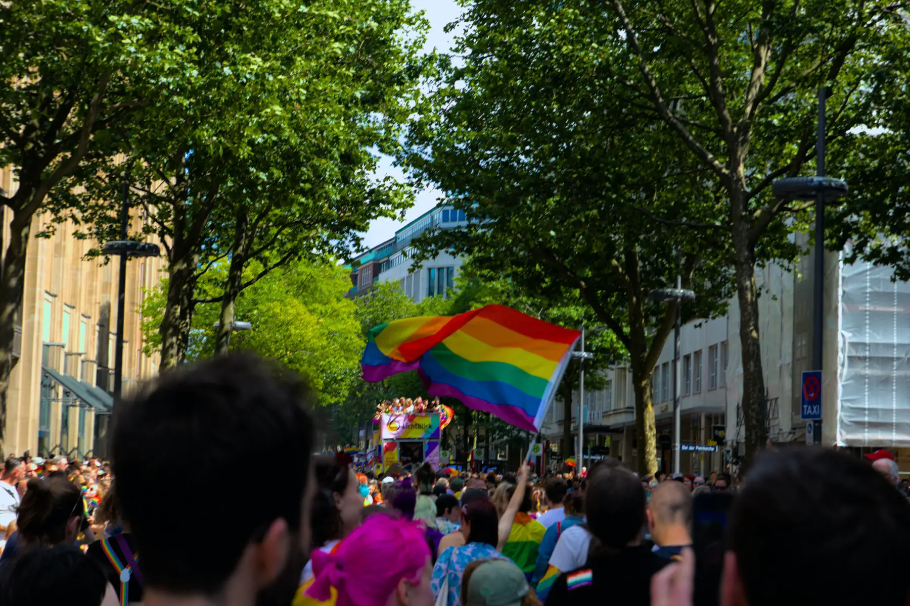 Crowds of people marching along the streets on Hamburg waving an LGBT flag in celebration of Hamburg Pride