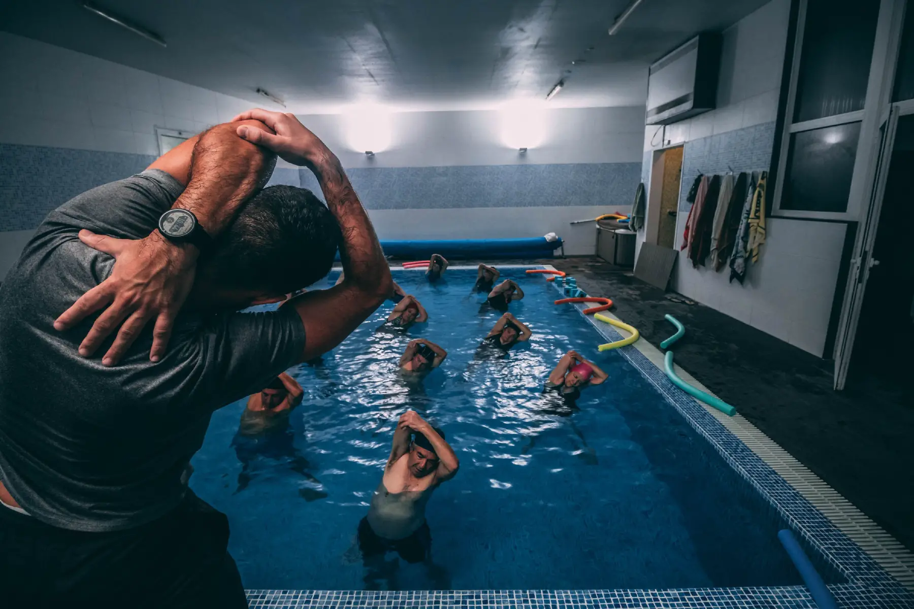 Instructor leads water aerobics class in indoor pool