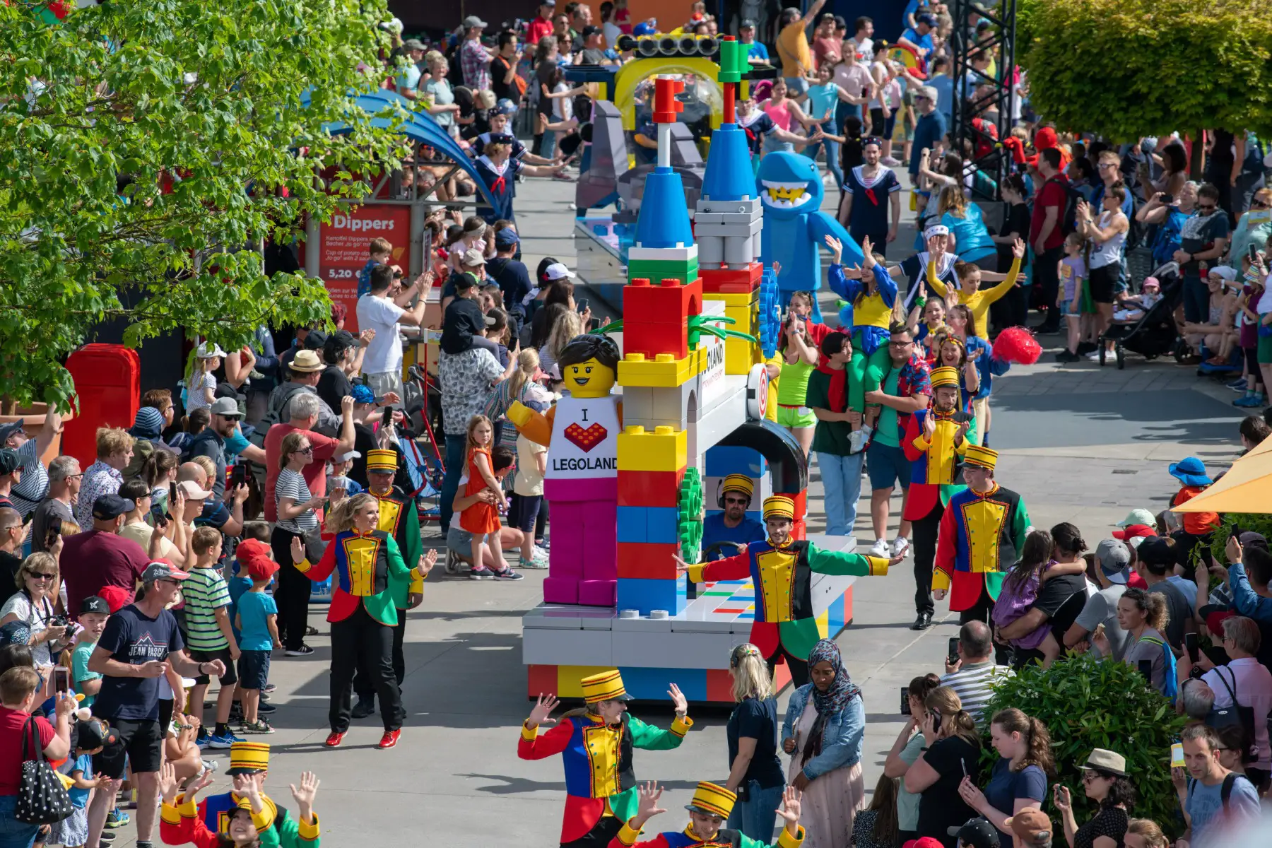 a parade of colorful characters walking through Legoland with crowds cheering on either side