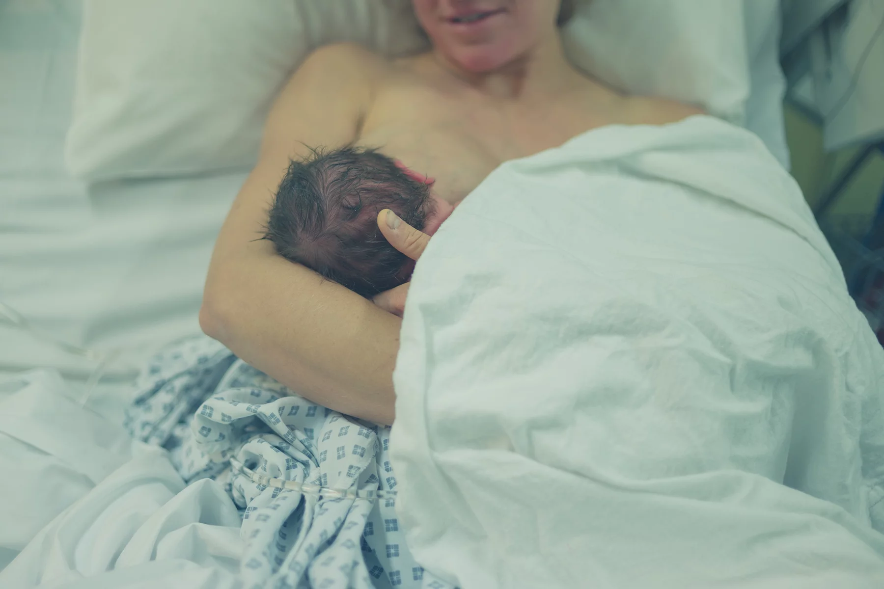 A mother smiles at her newborn as she breastfeeds for the first time lying together in the hospital bed