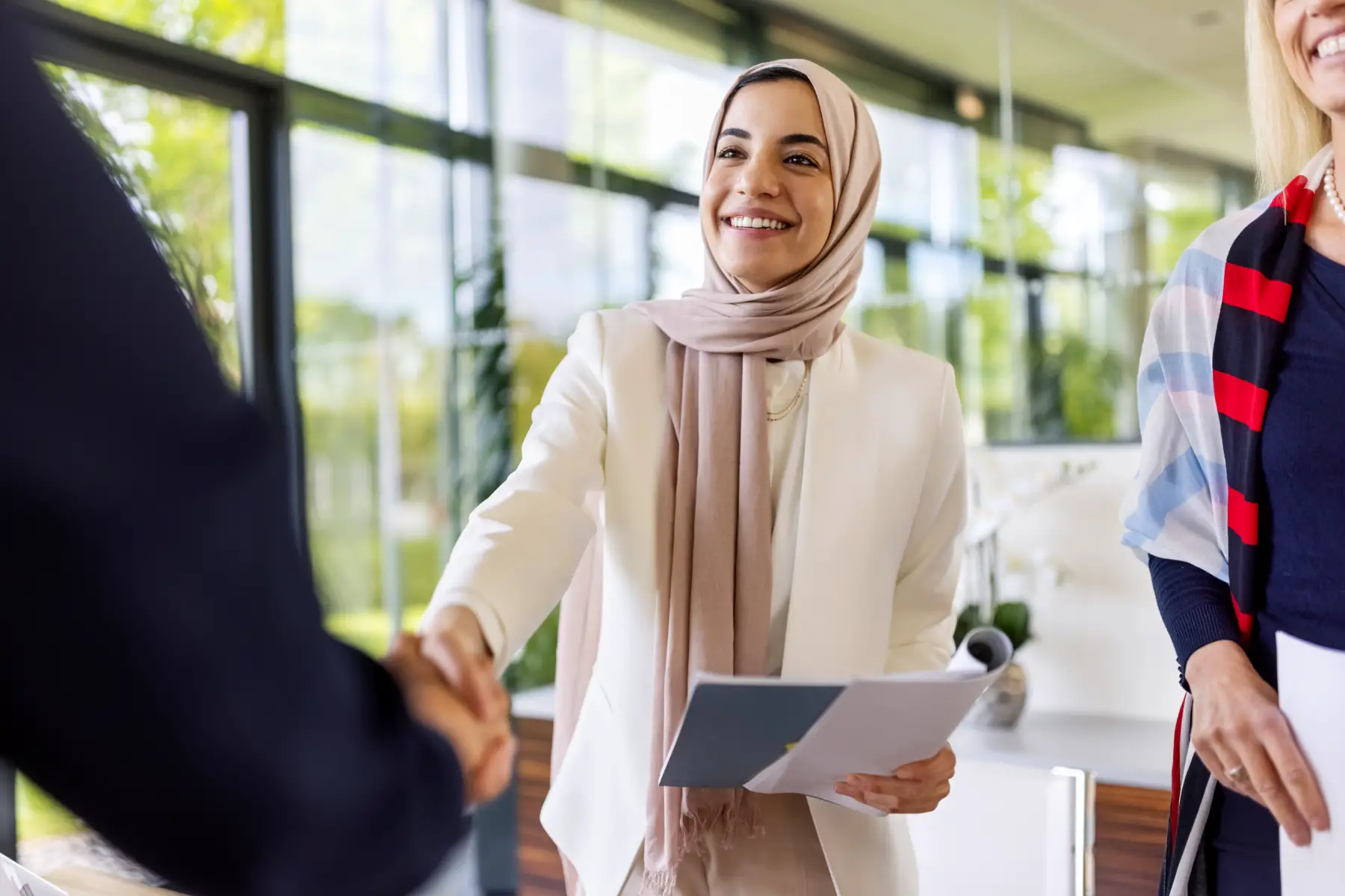 Woman wearing headscarf smiles and gives a handshake in an office