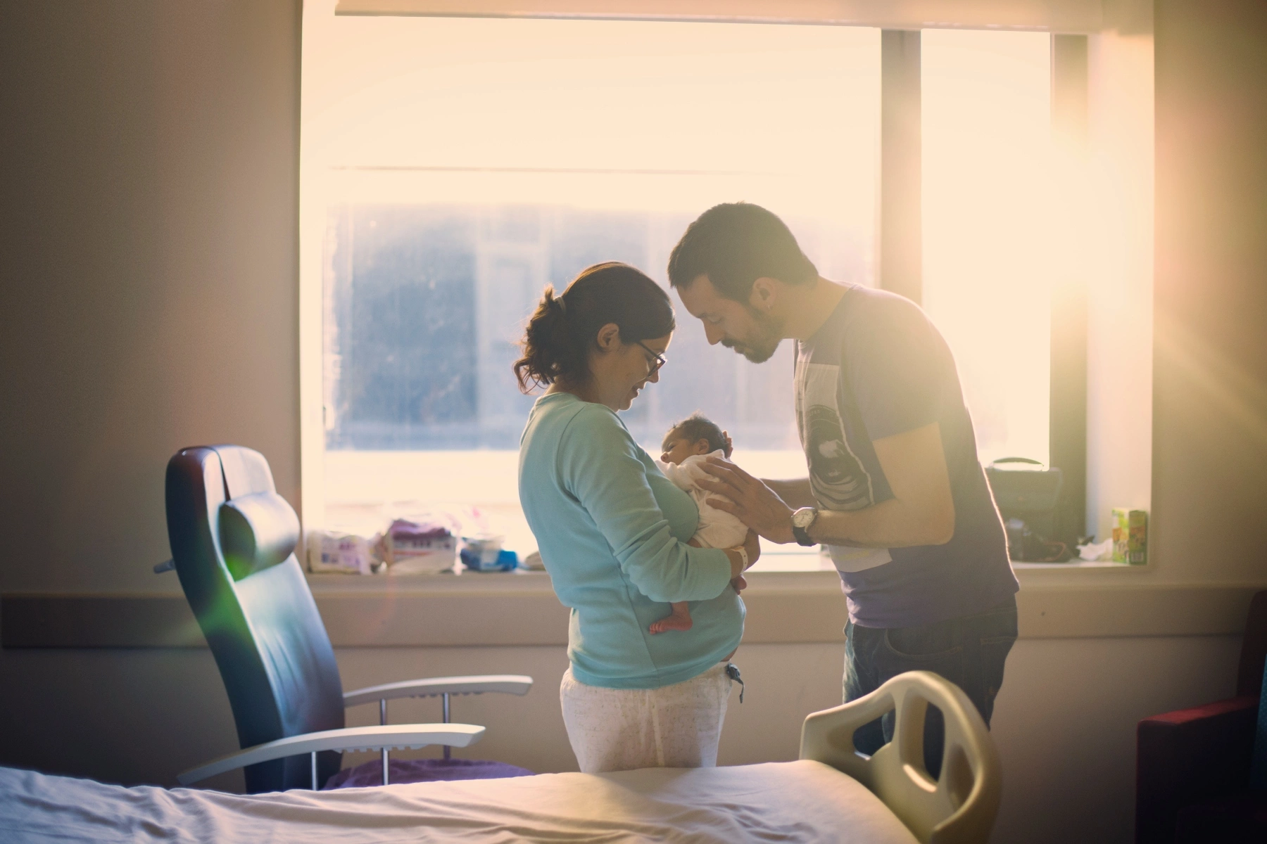 parents holding a newborn baby in a hospital room and looking at it lovingly