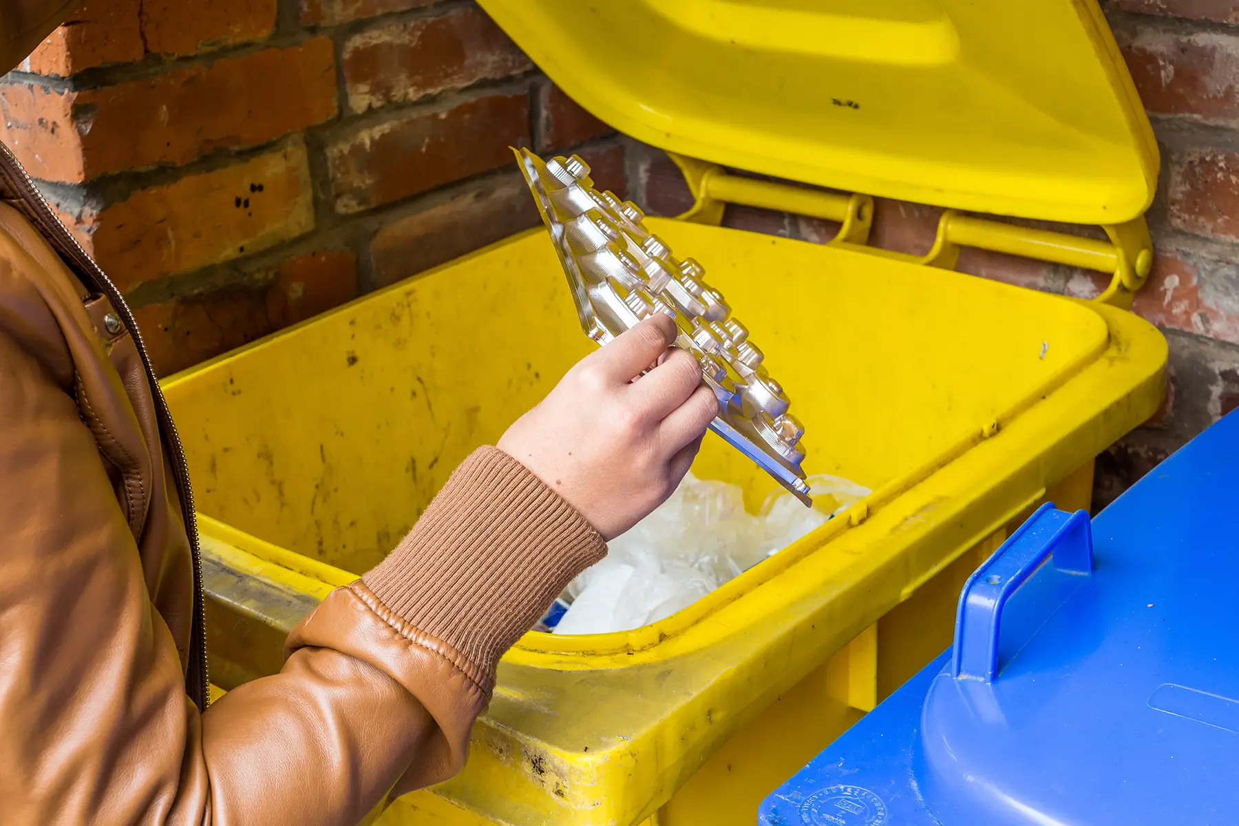 A person puts some packaging into a yellow bin