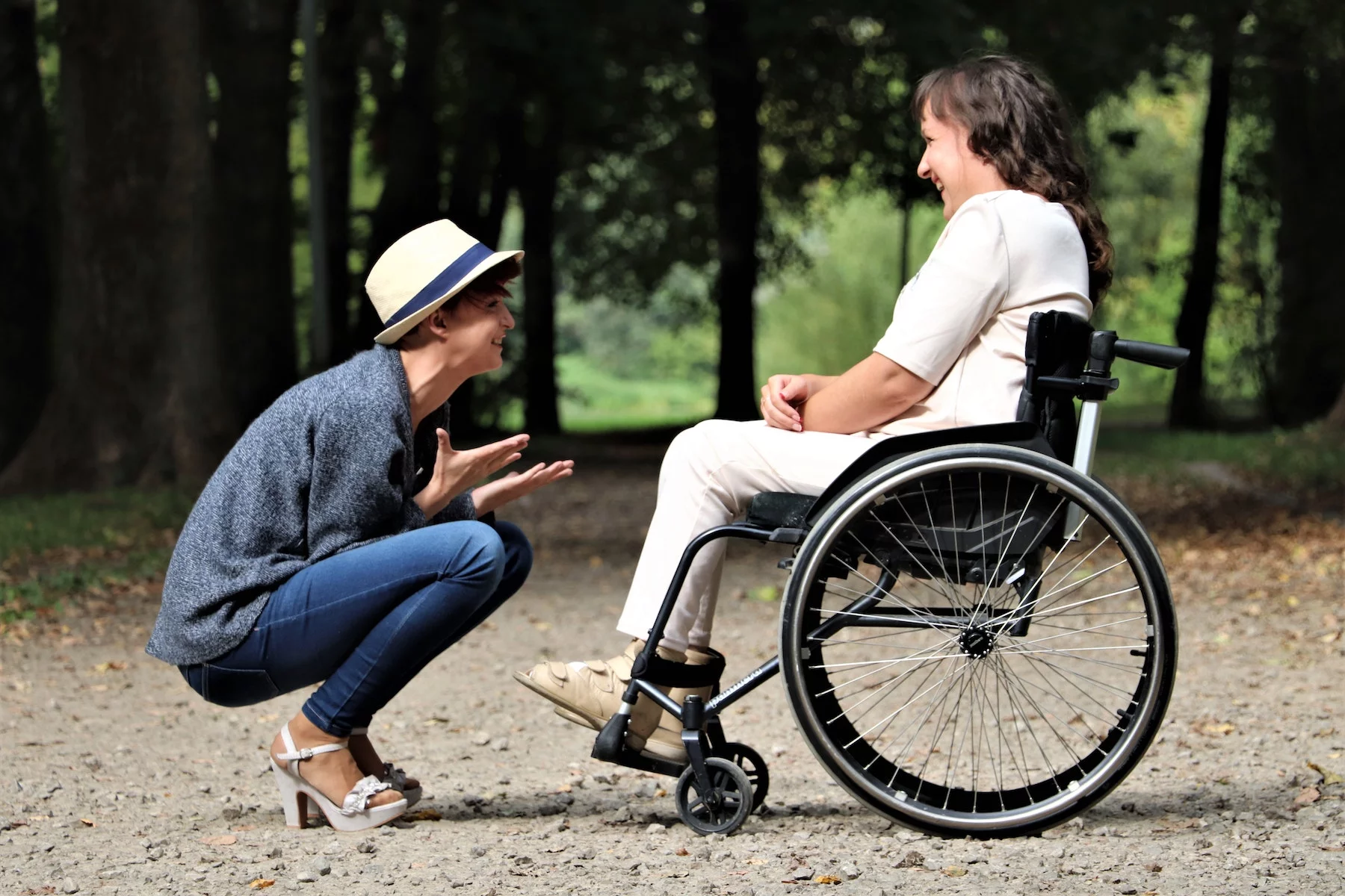 Person squats on the ground to talk to friend in a wheelchair, both are laughing
