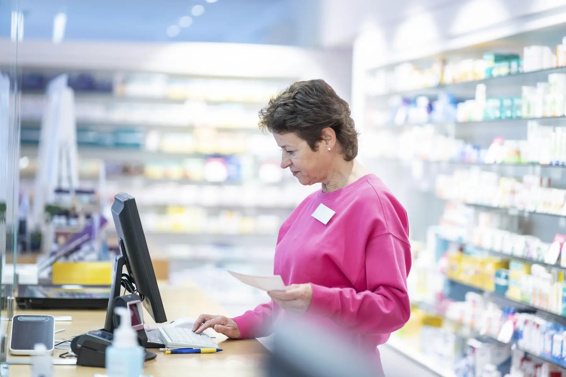 Pharmacist behind the counter enters prescription information into a computer
