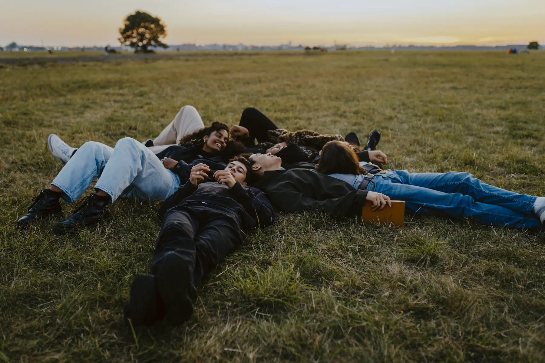 A group of teen friends are lying in the grass together talking just before sunset.