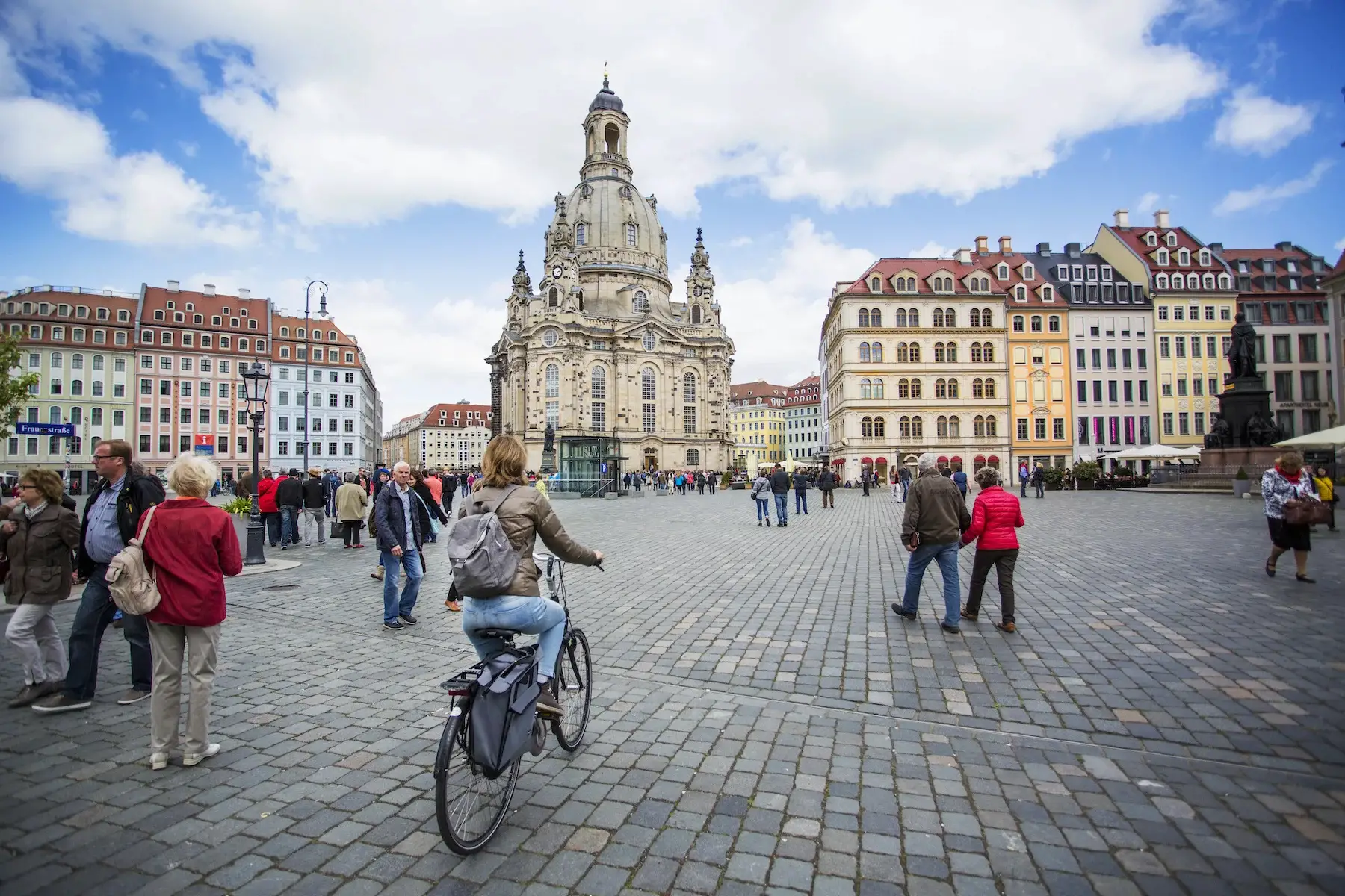 A woman cycles through Dresden's market square with a church towering in the background