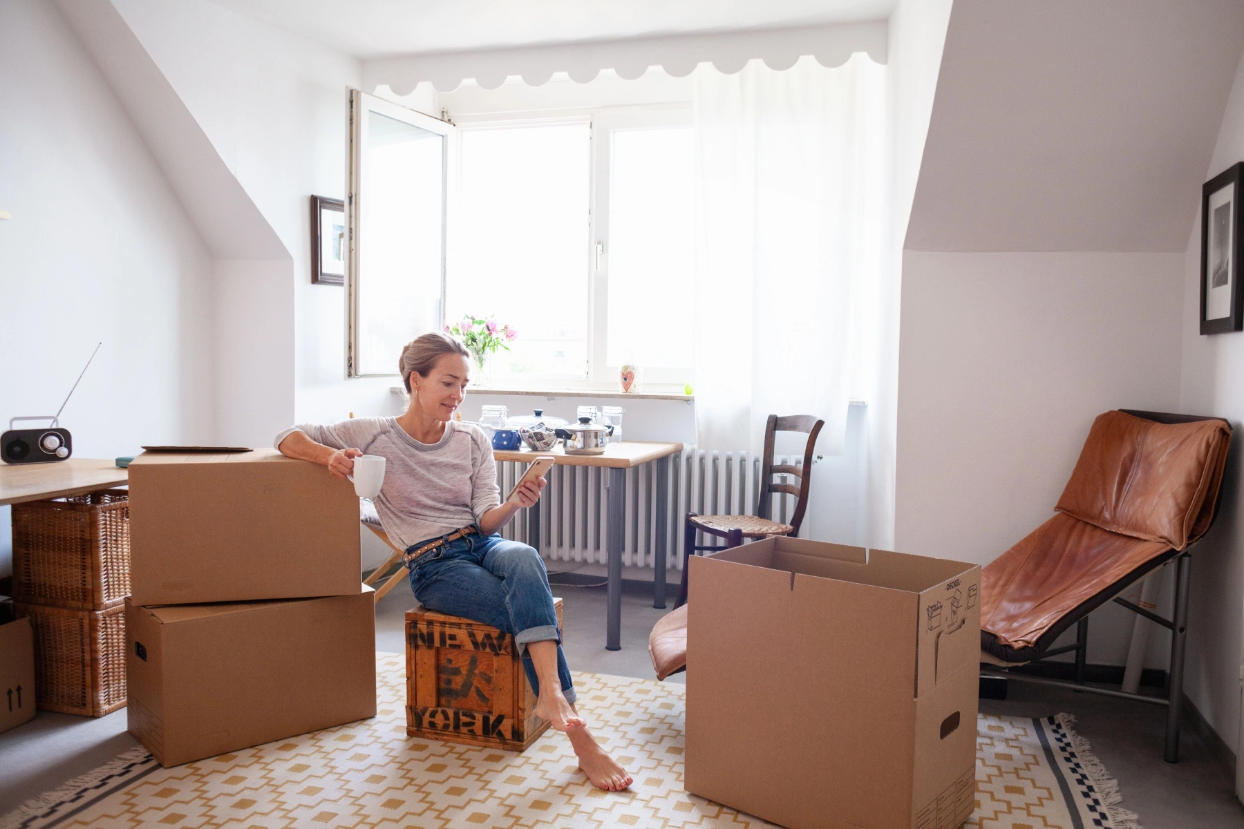 Woman checking her phone and sitting amidst moving boxes