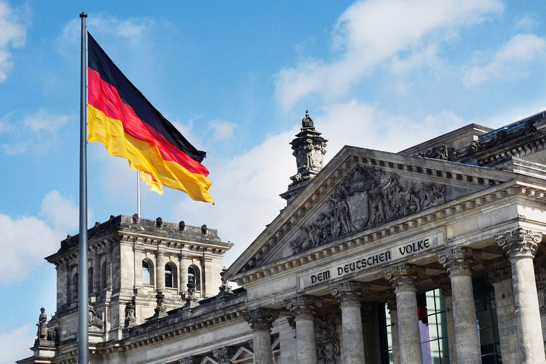 Large German flag is flying over the Platz der Republik in Berlin, Germany. The building reads "Dem Deutschen Volke".