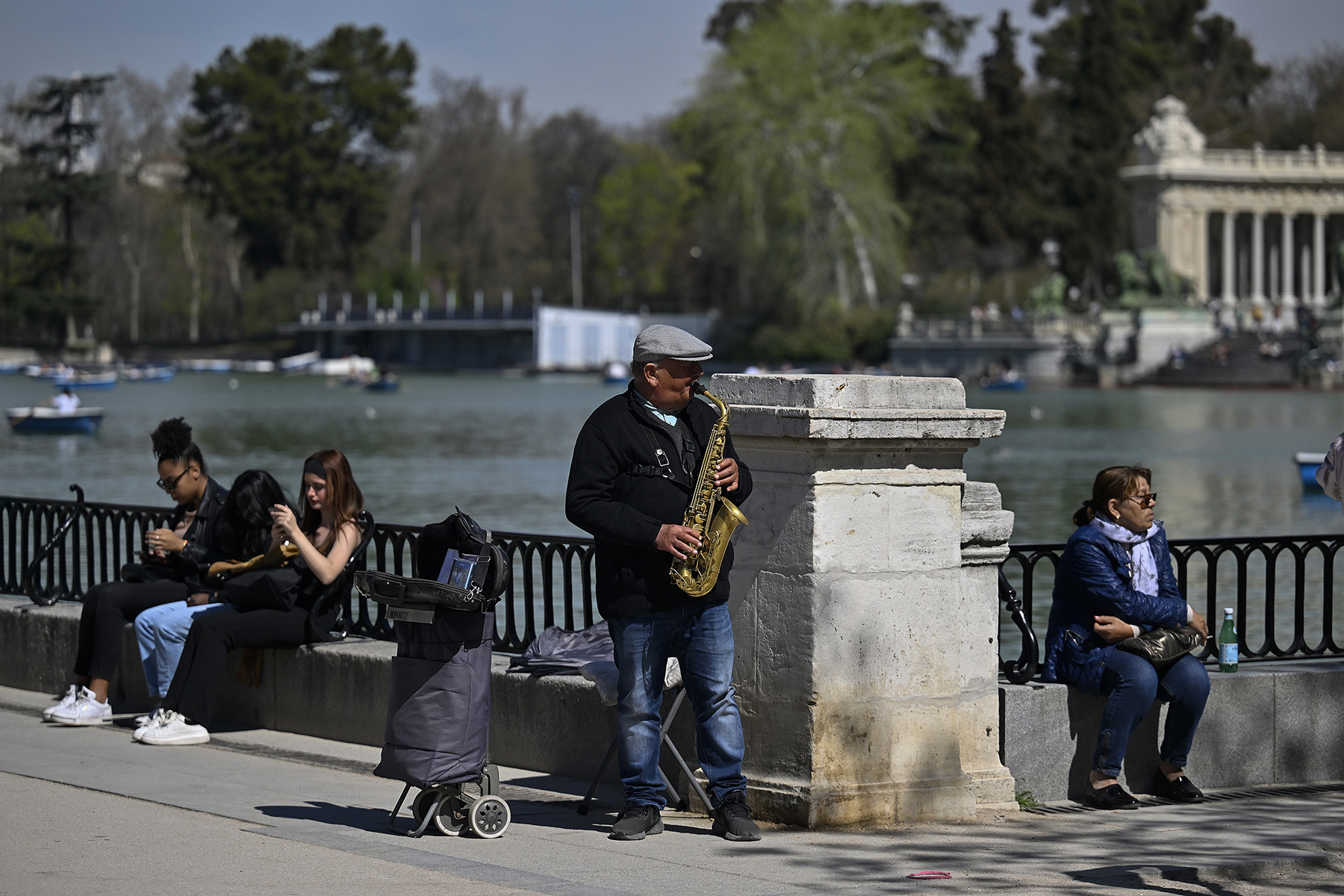A street musician playing saxophone next to a lake in Parque de Retiro in Madrid on a sunny day