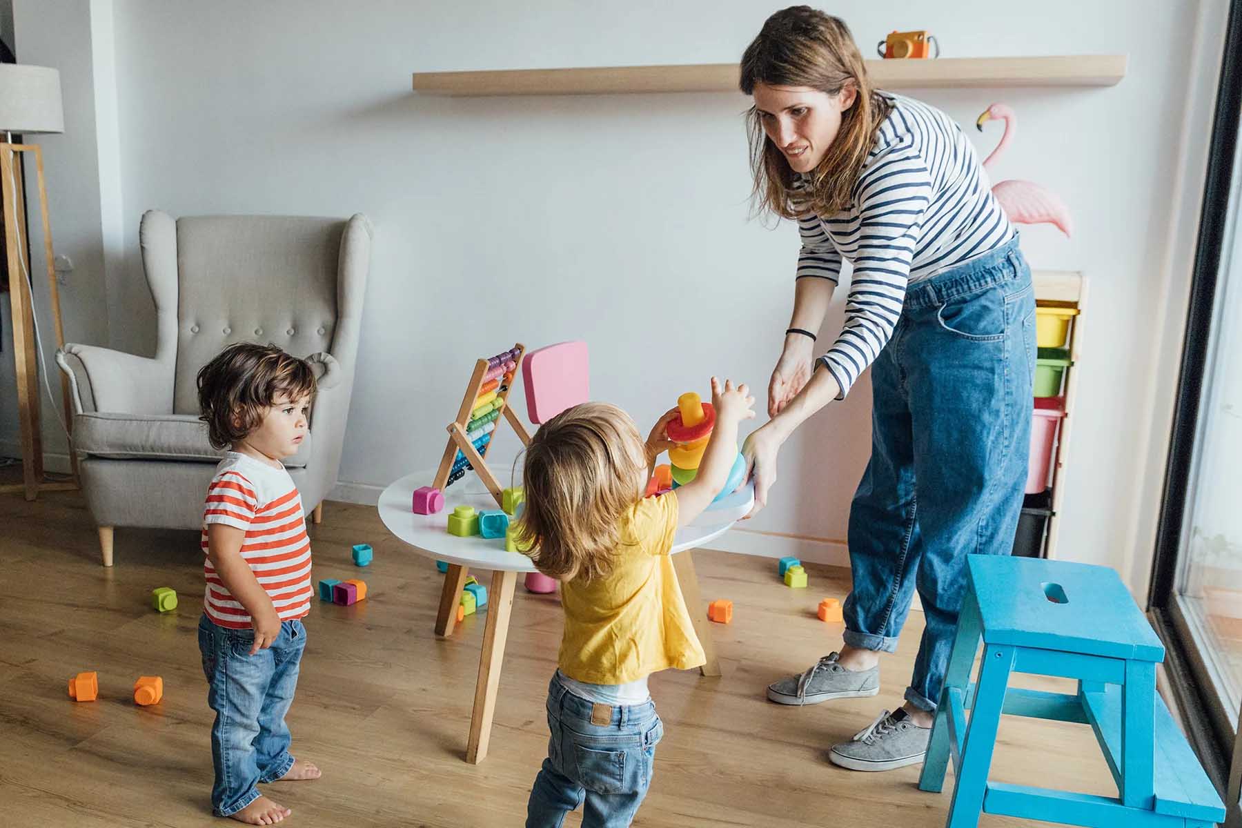 A preschool teacher with two children in a classroom, toys around the room