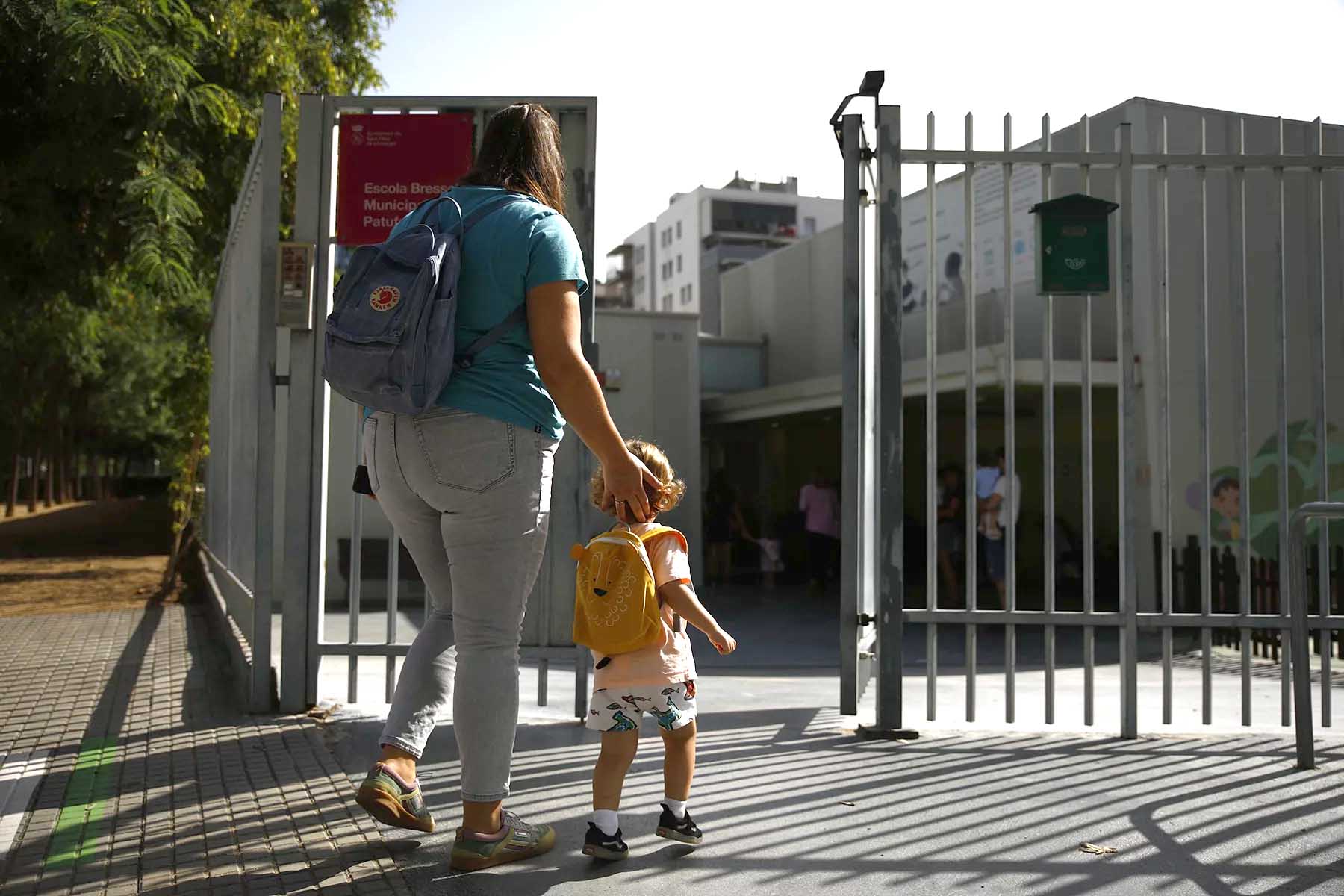 A mother walking into a Spanish preschool gate with her child.