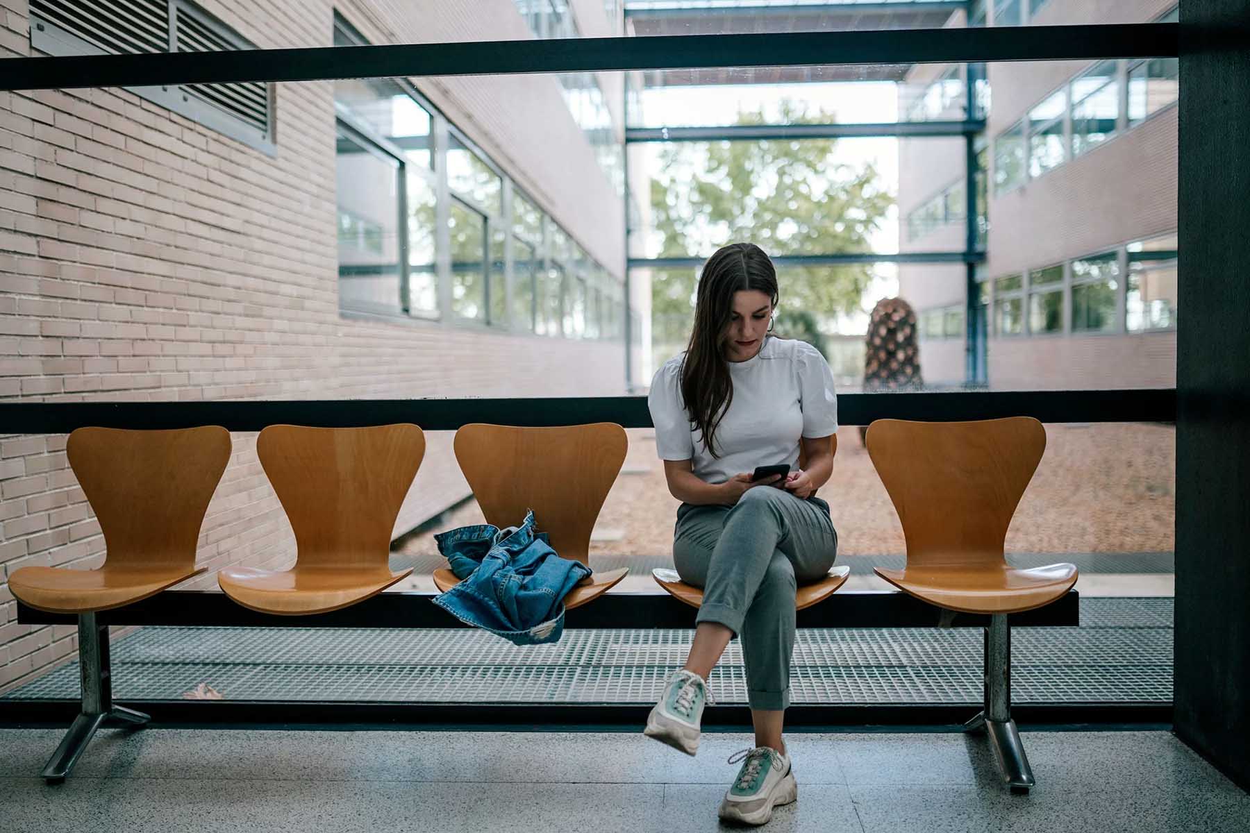 A student sits in a university corridor looking at her phone