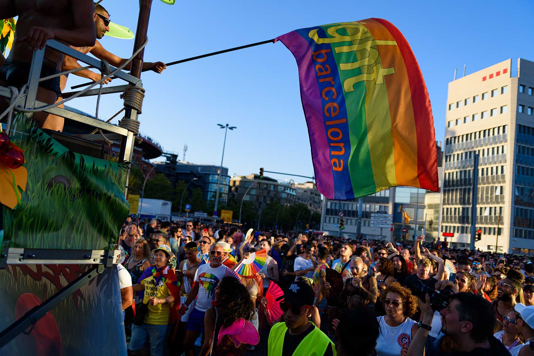 A man standing on top of a bus waves an LGBT flag during the 2023 Pride parade in the Barcelona city center. 