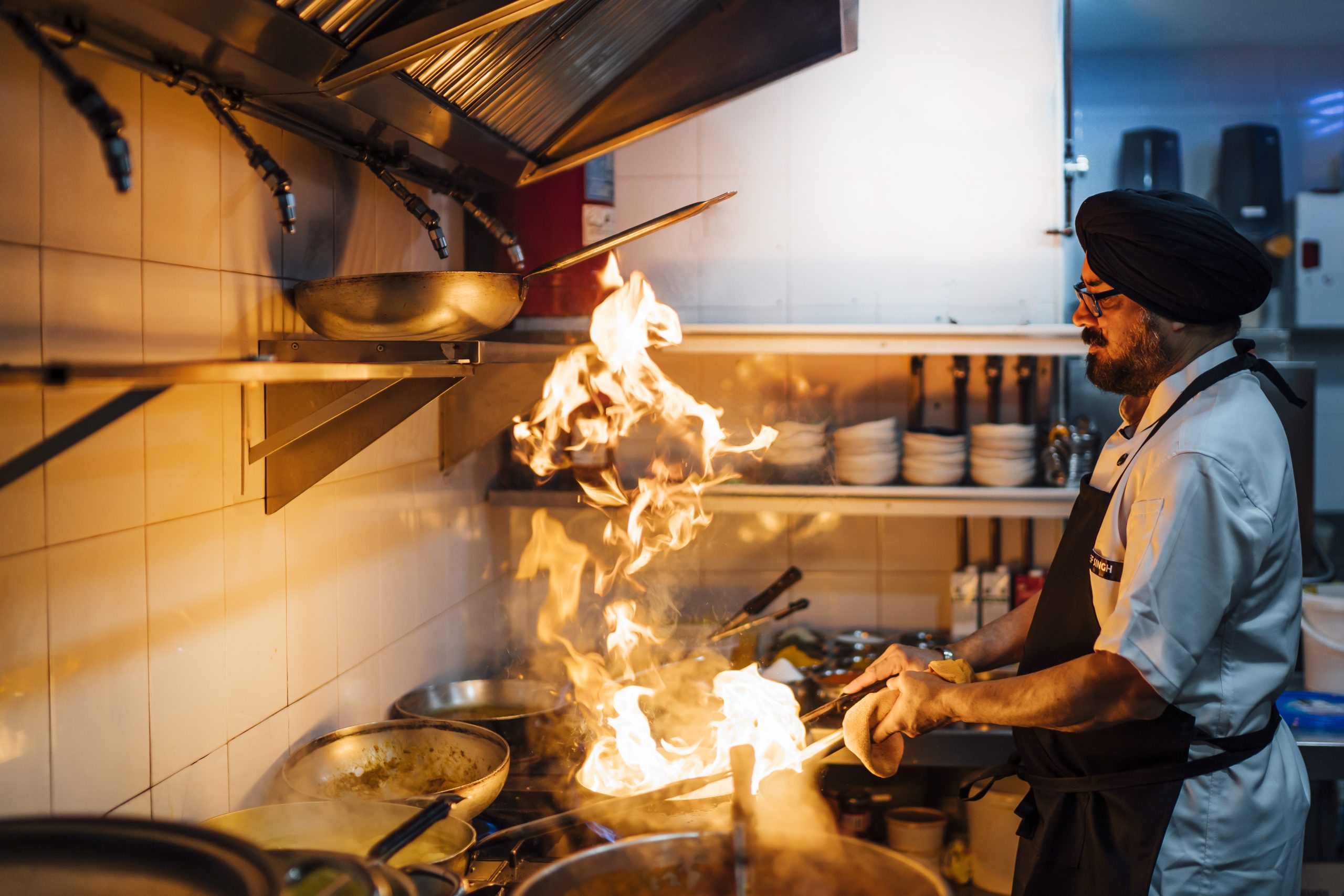 Indian chef flaming food in restaurant kitchen in Madrid.