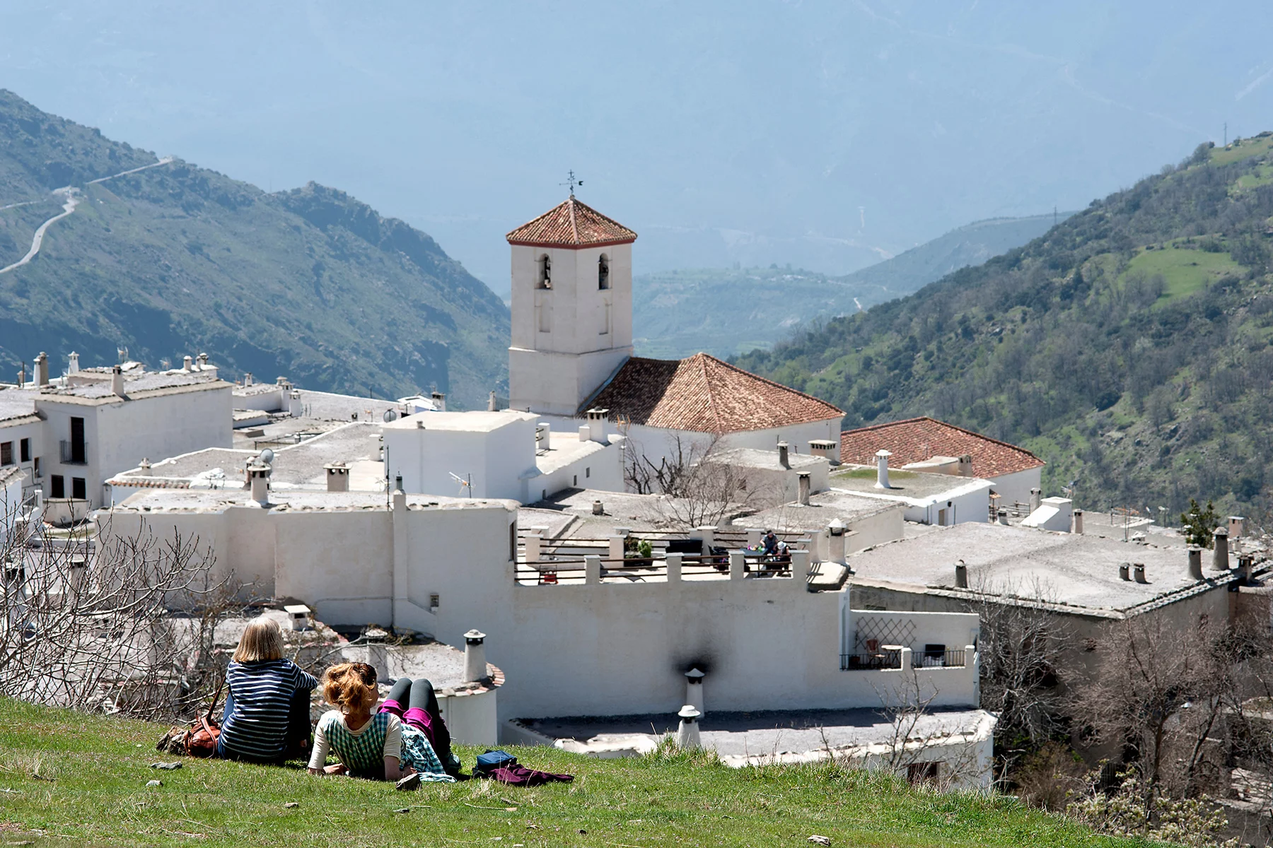 Tourists sitting on a hill looking at the village of Capileira in Andalucia