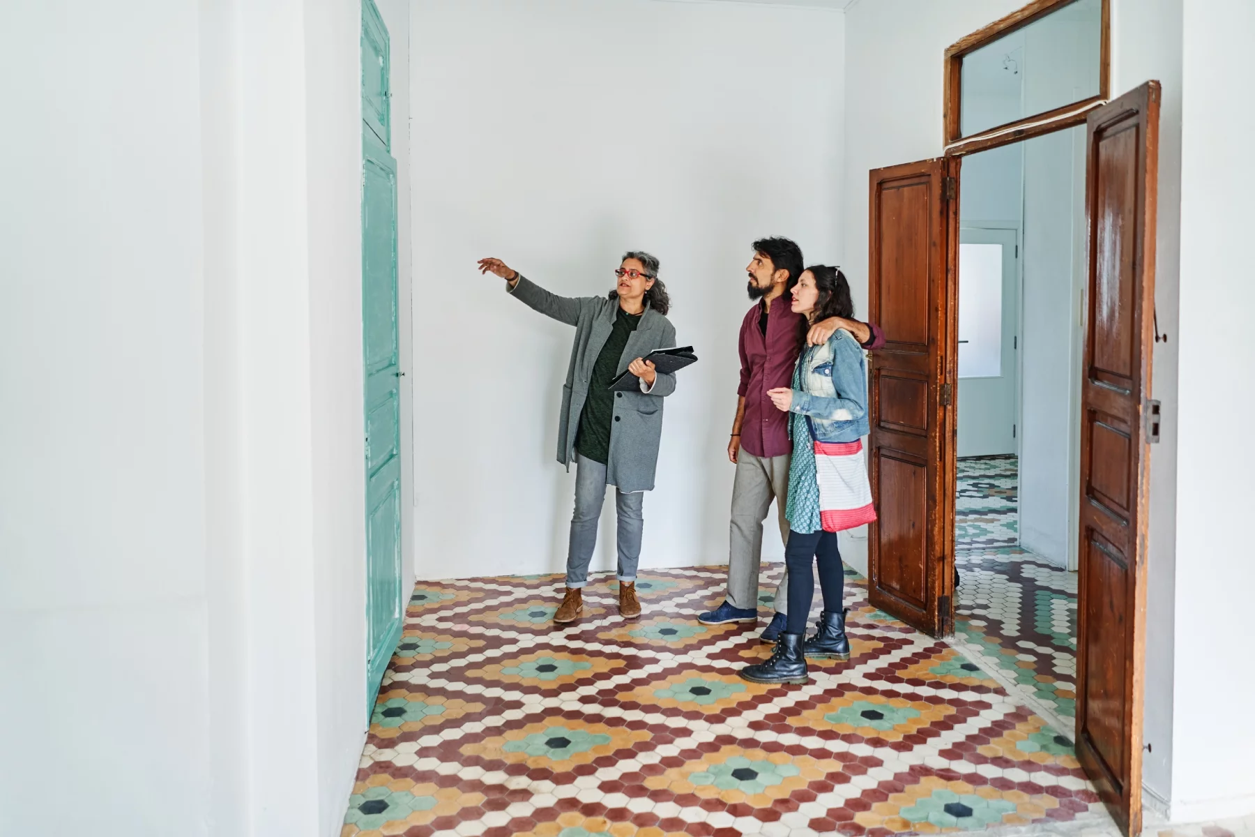 An estate agent showing a couple around a flat in Valencia. White walls, colored tiled floor.