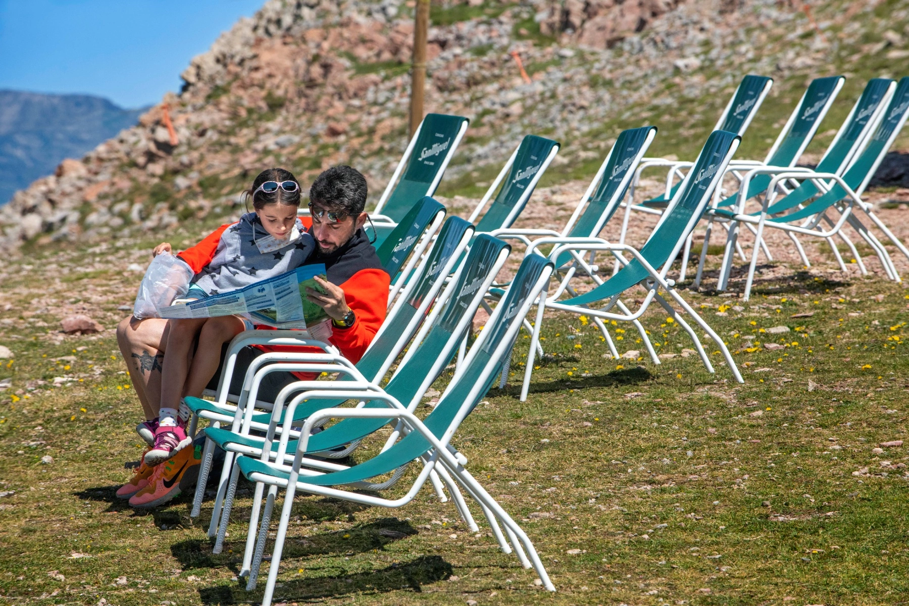 Father and child look at map while sitting on deckchair at La Molina ski resort