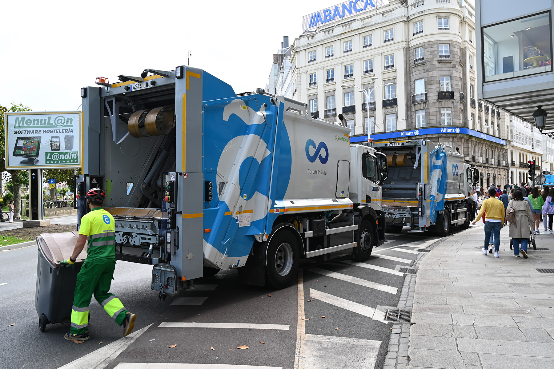 Garbage trucks on a busy street with garbage collectors in La Coruña, Spain
