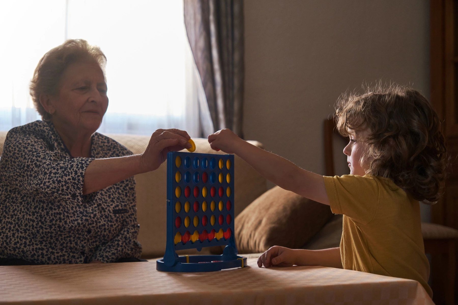 Grandchild and grandmother play Connect Four indoors