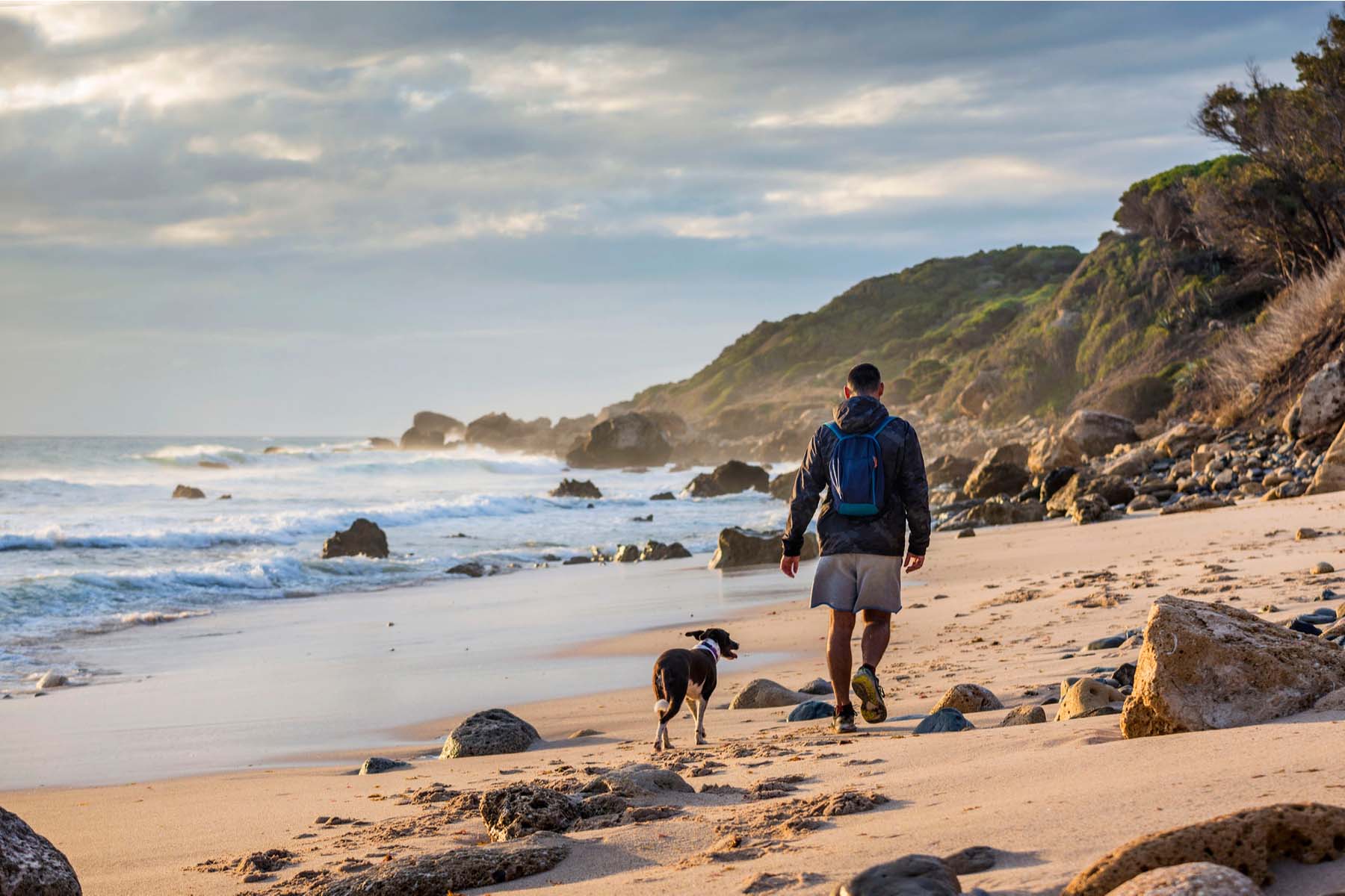 man walks dog along deserted beach in Spain