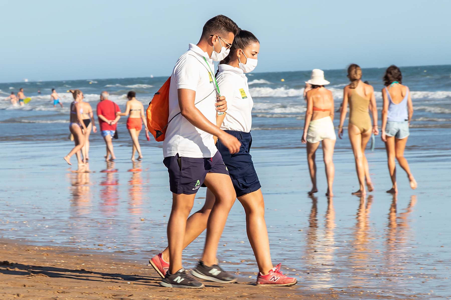 couple walking on beach wearing masks