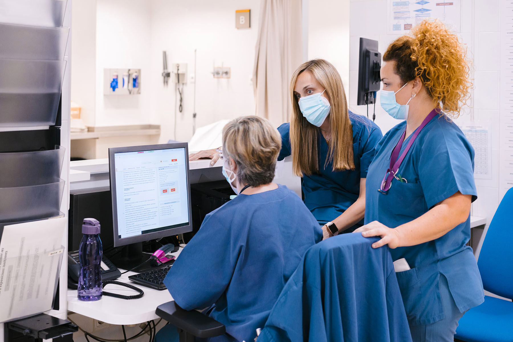 Nurses wearing protective face mask having discussion at around a computer.