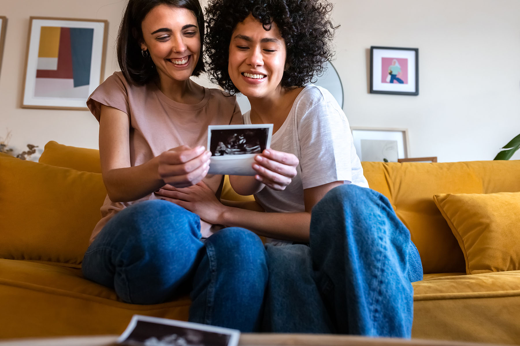 Pregnant couple looking at a baby ultrasound, sitting at home on the sofa.
