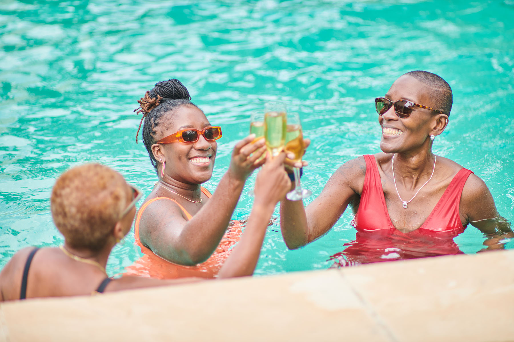 Three women in a swimming pool, smiling and toasting their champagne.
