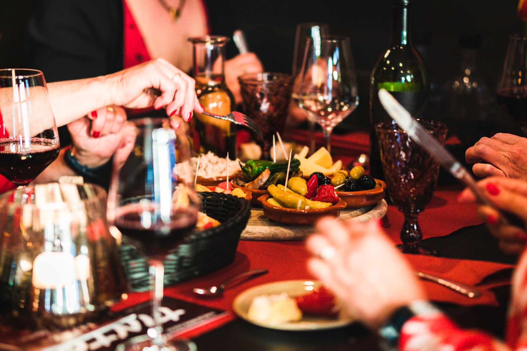 a close-up shot of friends eating tapas around a table with wine glasses placed next to the dishes