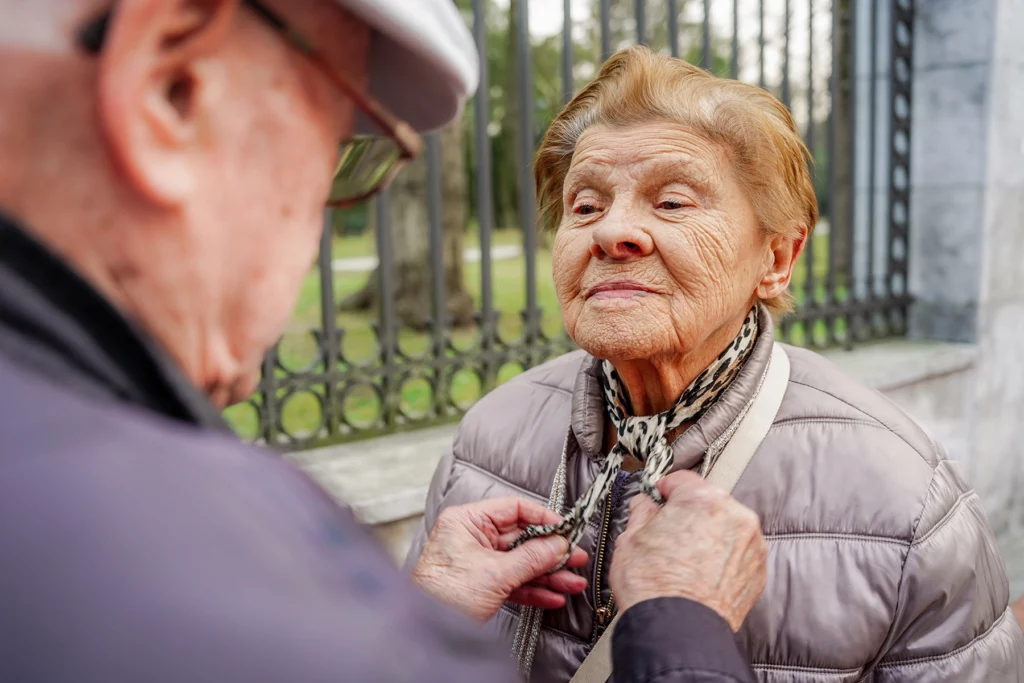 A senior man helping this wife with dementia to dress - health insurance for seniors in Spain