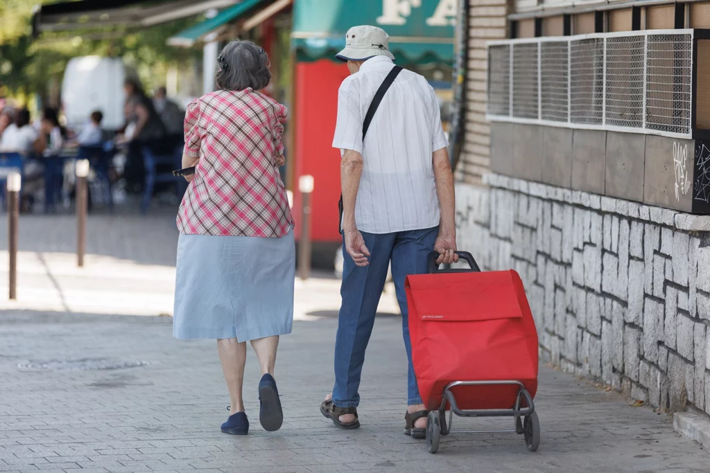 44Older couple walks down street with shopping trolley