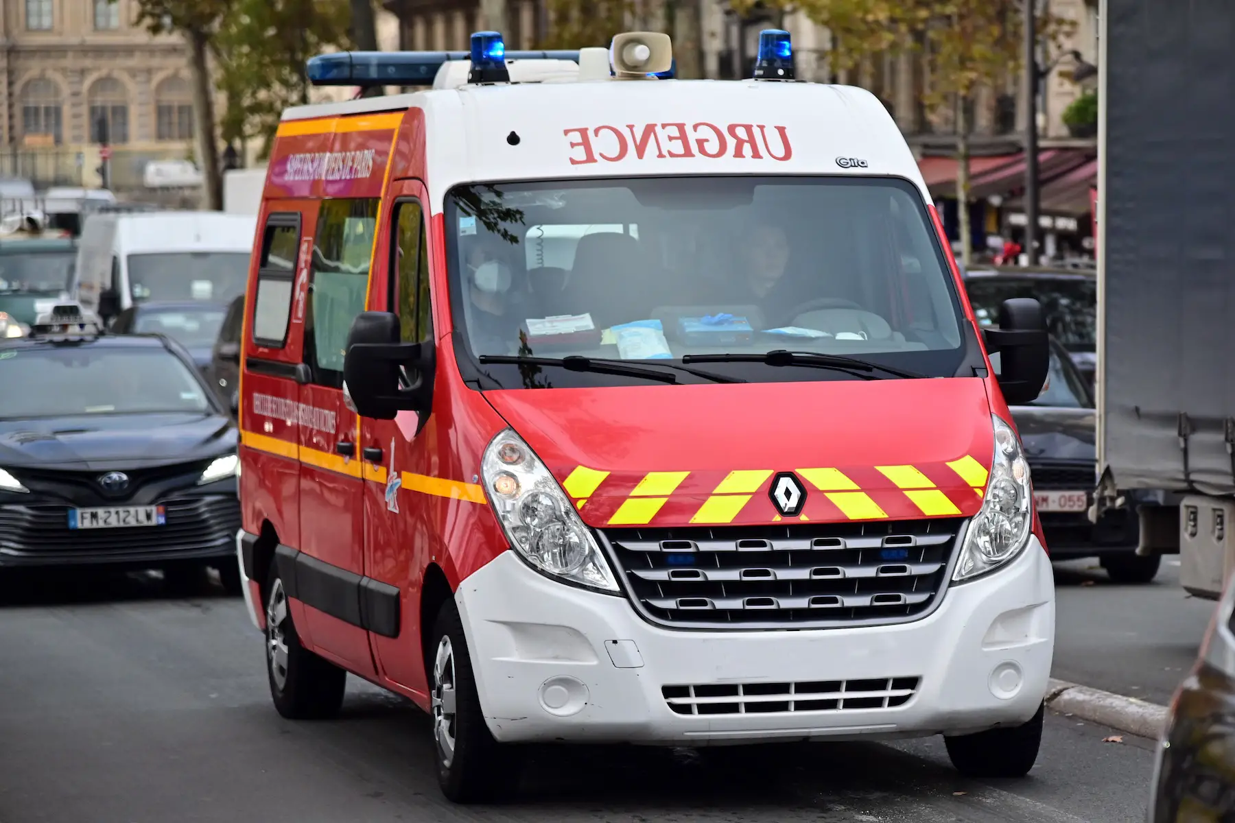 An ambulance drives down a busy Paris street with its blue emergency lights turned on