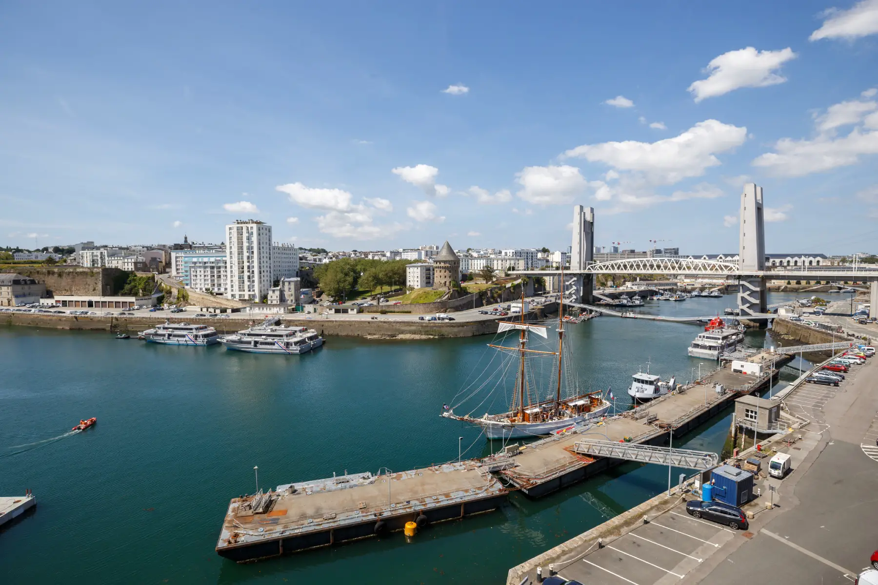 a view of the cityscape in Brest on a clear sunny day with boats lining the harbor and tall building in the background
