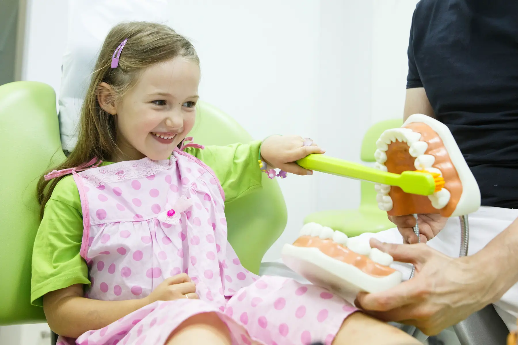 a little girl visiting the dentist and brushing a giant model of teeth