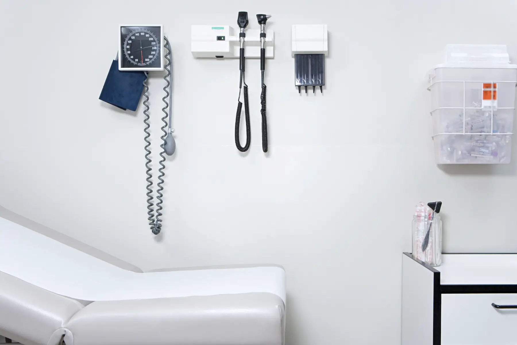 The wall of an empty doctor's office exam room is shown, with a blood pressure monitor and various other equipment on display