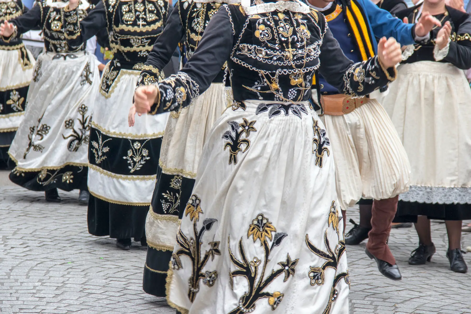 a group of women dressed in black and white folkloric robes dancing along the street at a festival in Brittany