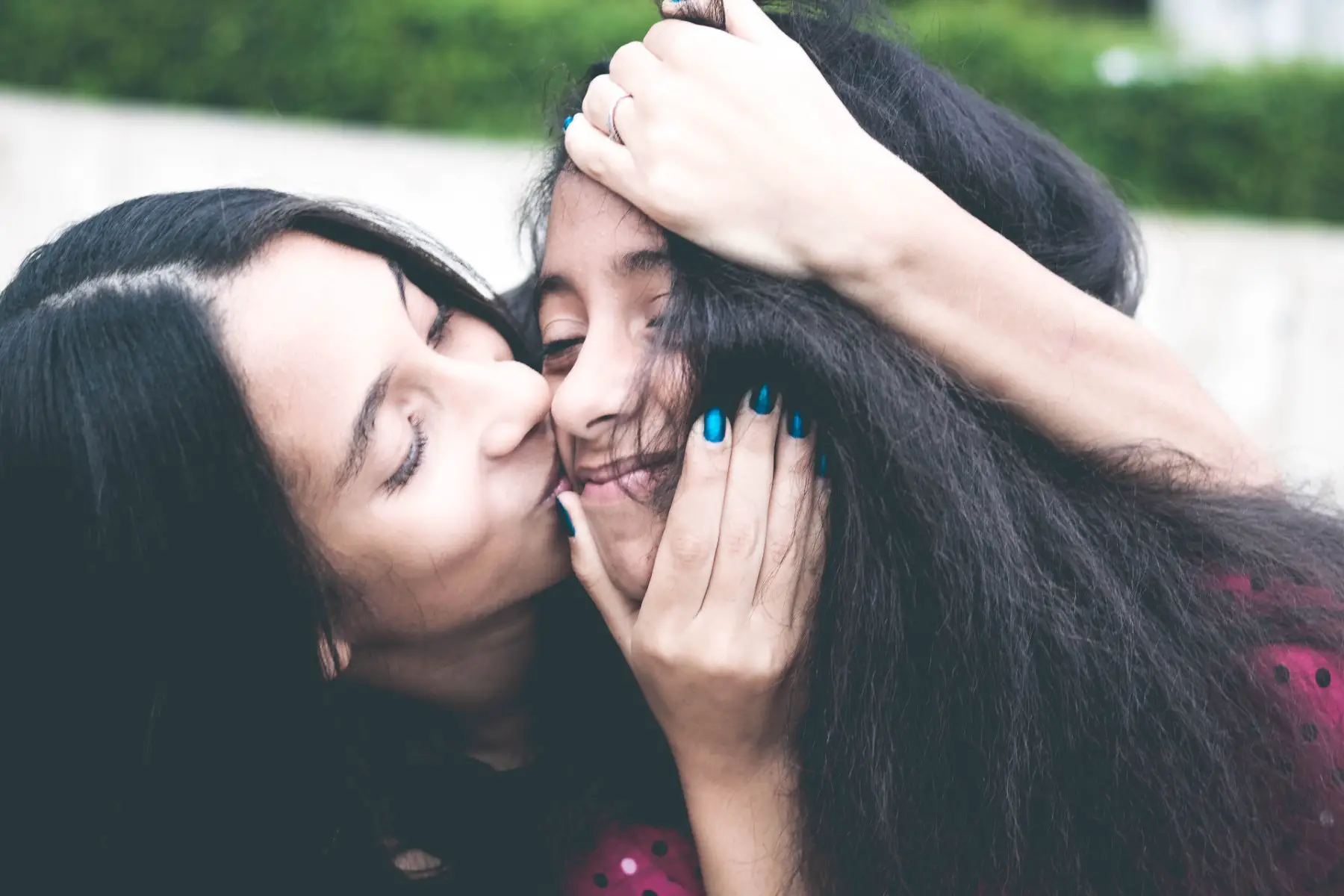 Woman holding girl's face and kissing her cheek.