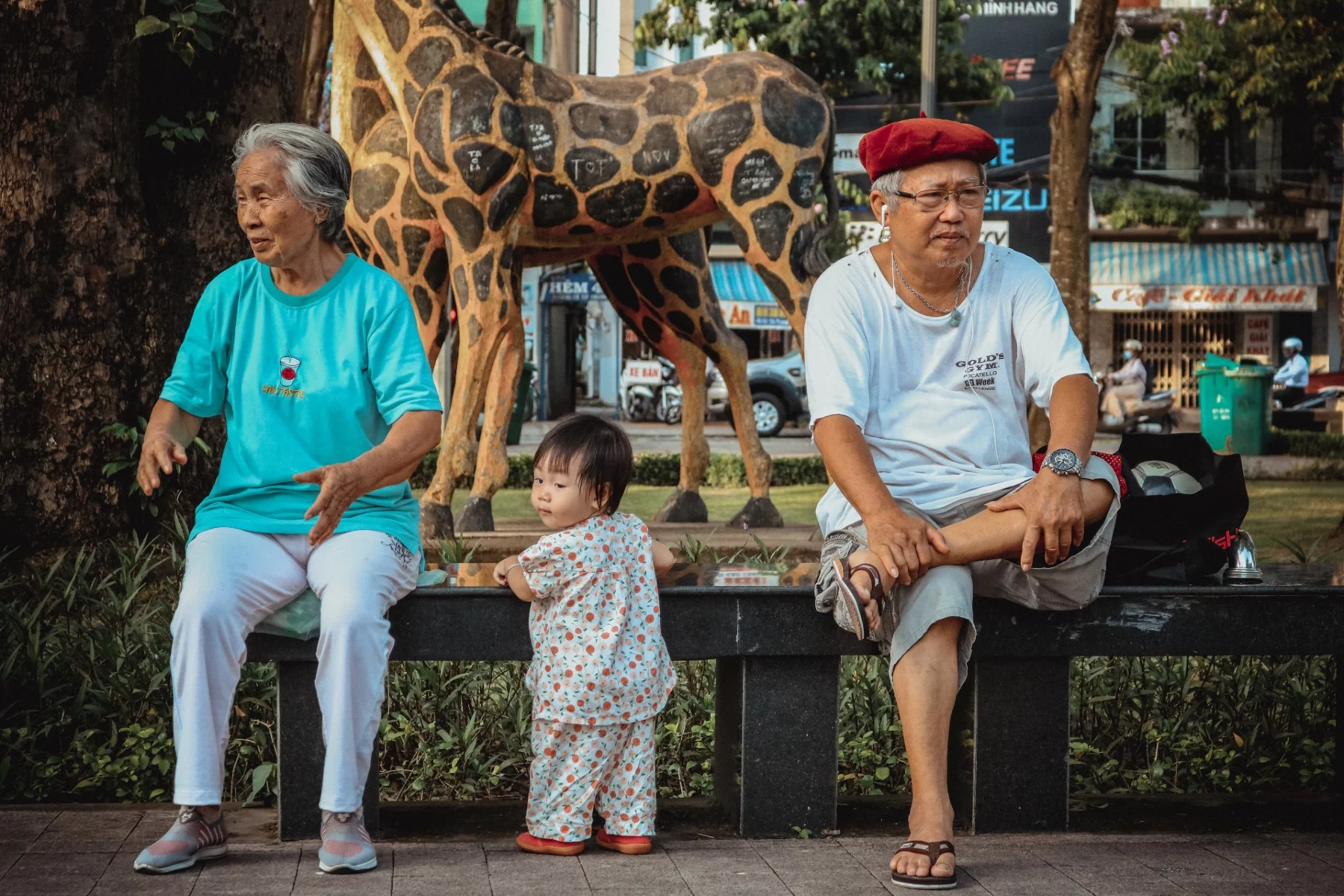 A toddler standing between her grandparents near the zoo. 