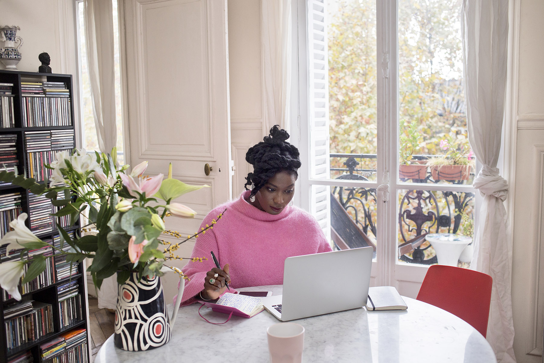 Lady in a pink jumper sitting in her apartment behind a laptop.