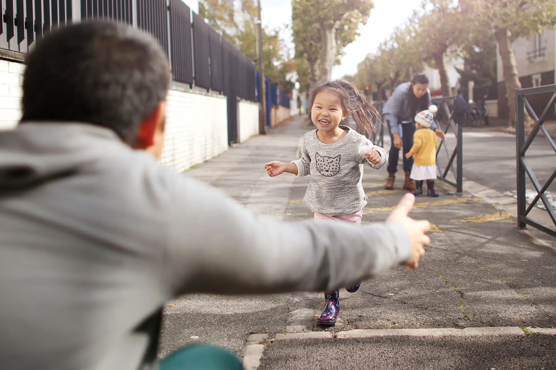 A smiling little girl running to the arms of her dad in the street.