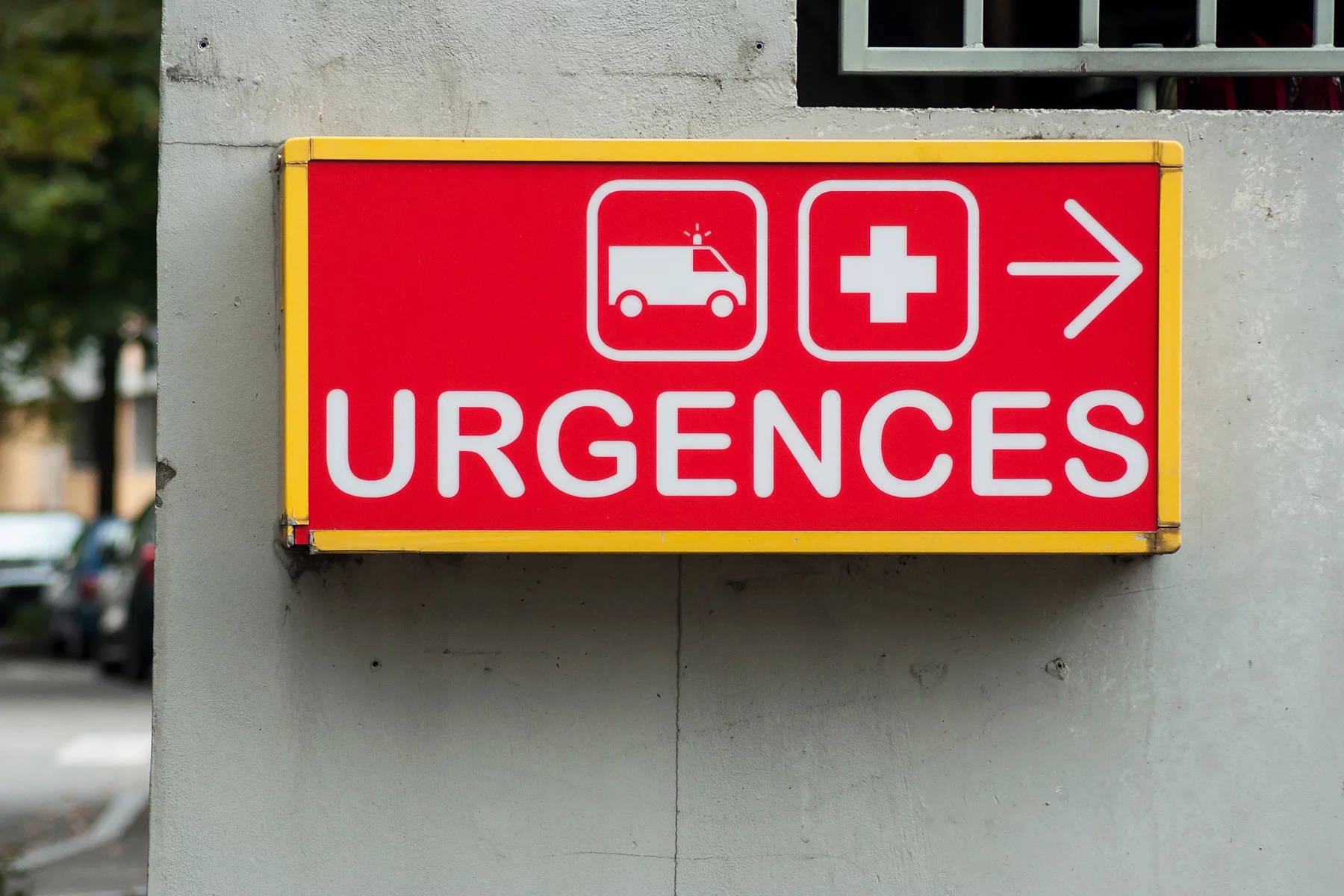 A bright red emergency room sign in France on the side of a concrete building