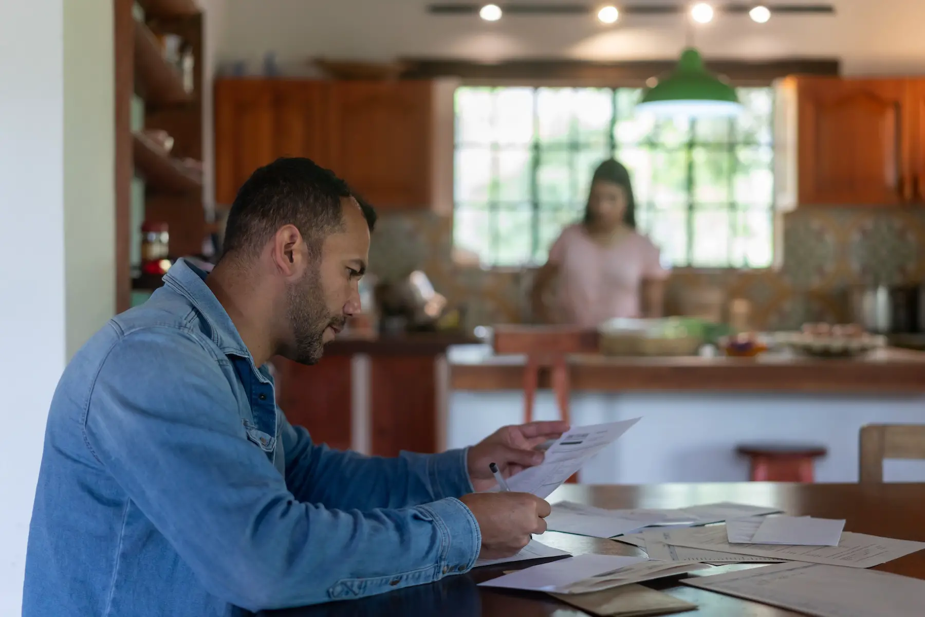 A man sits at his dining table looking over bills and documents while taking care of the home finances
